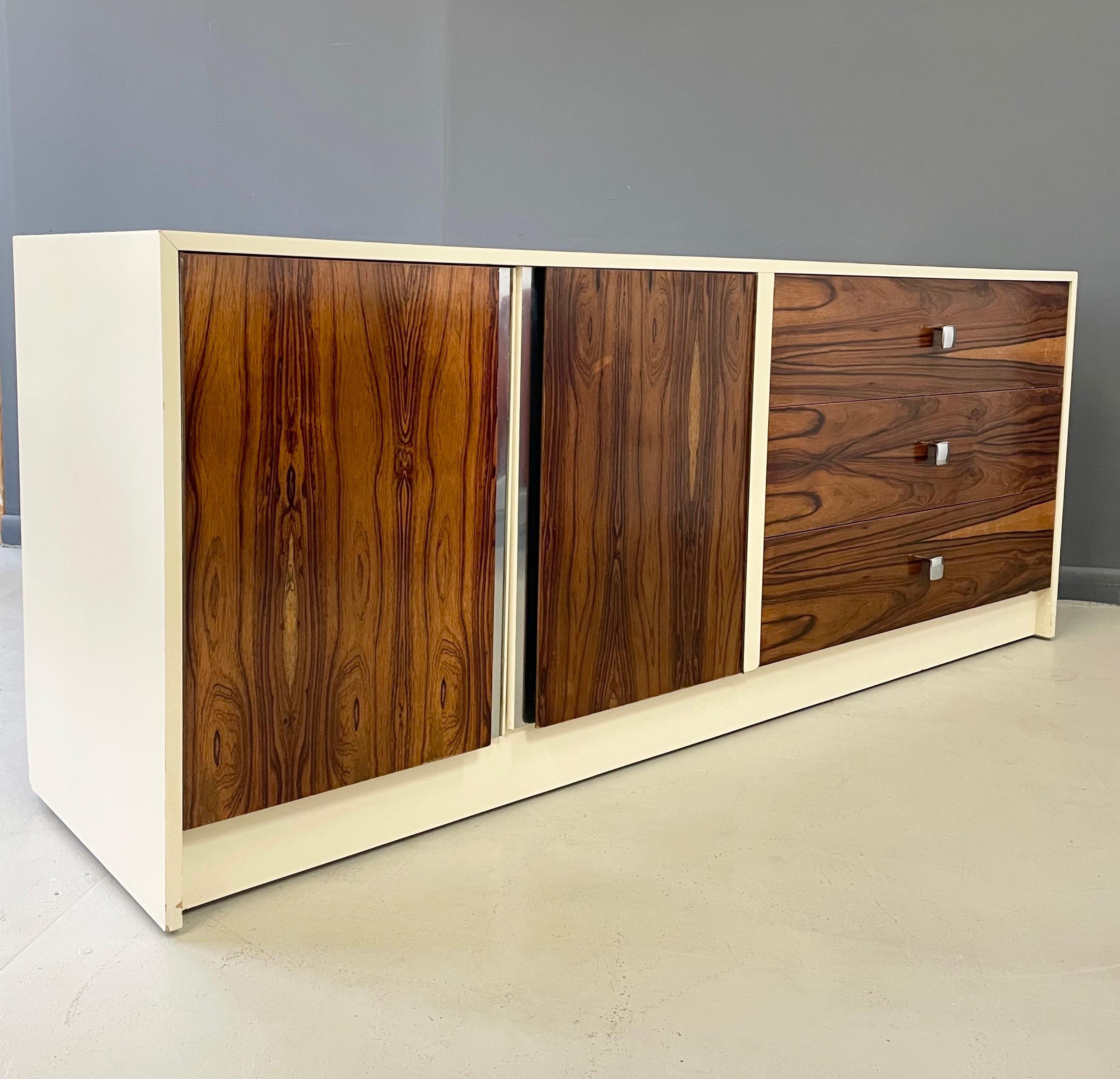 This credenza newly lacquered in white and having wonderfully grained three rosewood drawers and two doors that open to reveal one shelf is finished with chrome trim and stylish chrome pulls.