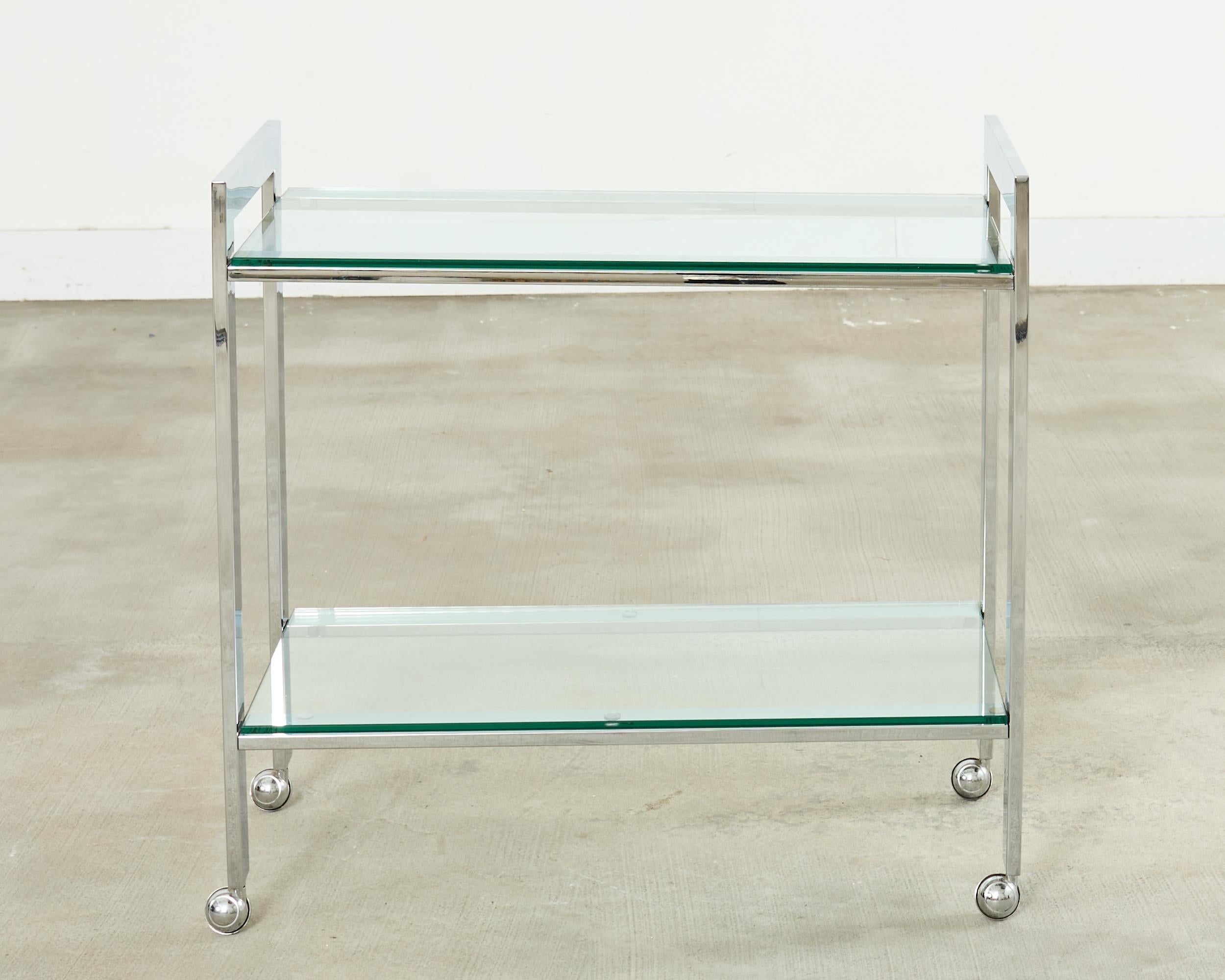 Stylish mid-century modern chrome and glass two tier bar cart made in the style and manner of Milo Baughman. The cart is constructed from flat bar steel with a thick shiny chrome finish. Each end has a U-shaped piece that forms the legs ending with