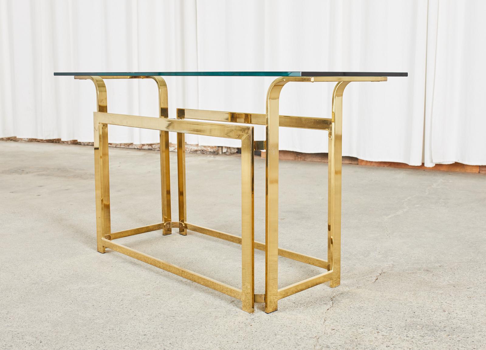 Mid-Century Modern console table or sofa table crafted from flat bar metal with a brass or gilded tone in the manner and style of Milo Baughman. The console features a rectangular frame with conjoined sides. The ends are gracefully curved upward