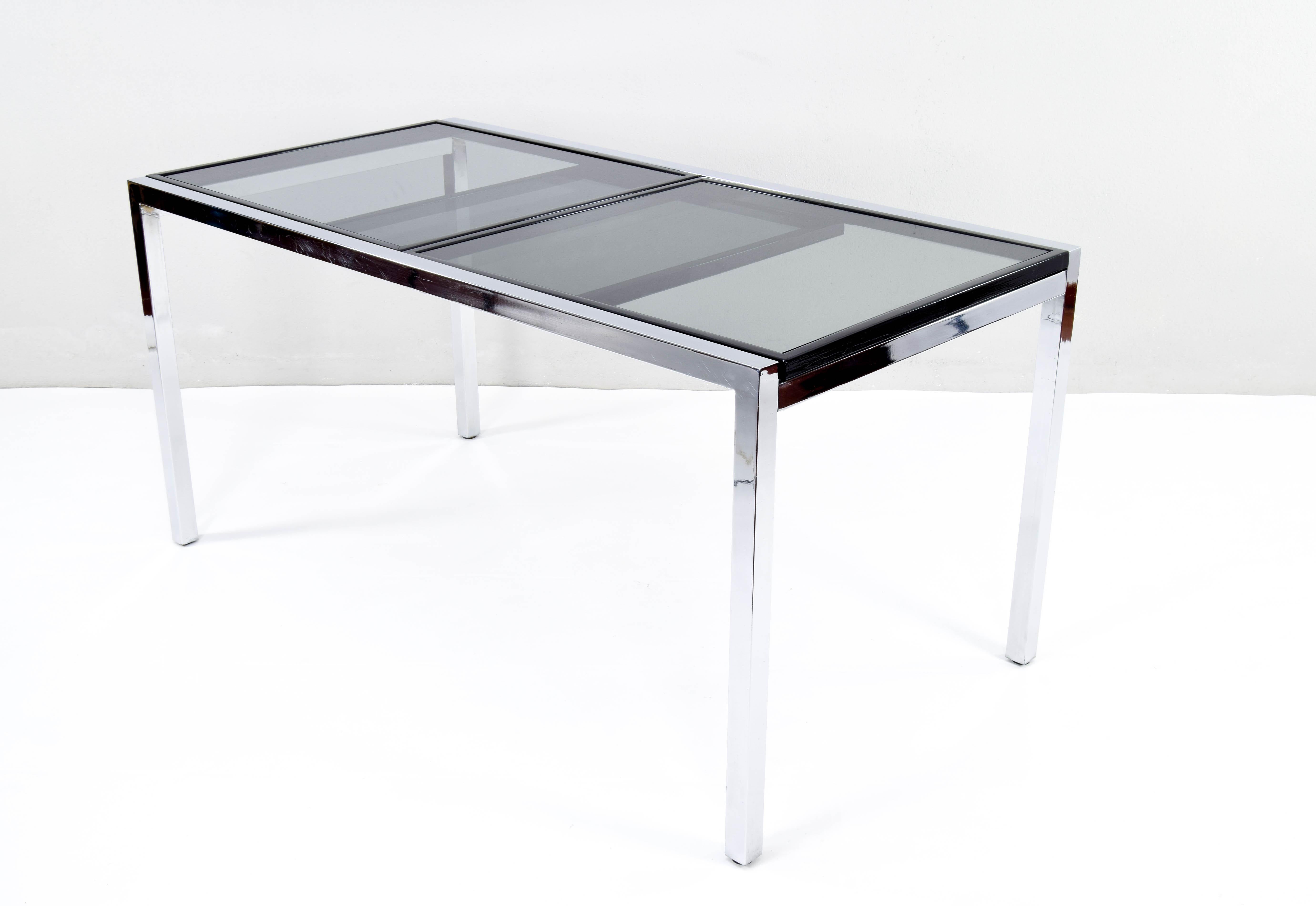 Extendable dining table designed by Milo Baughman. Manufactured in the 1970s. Its body is made of chromed steel and as in the first editions, the table comes with black lacquered wooden frames that support the three smoked glasses.
It is in very