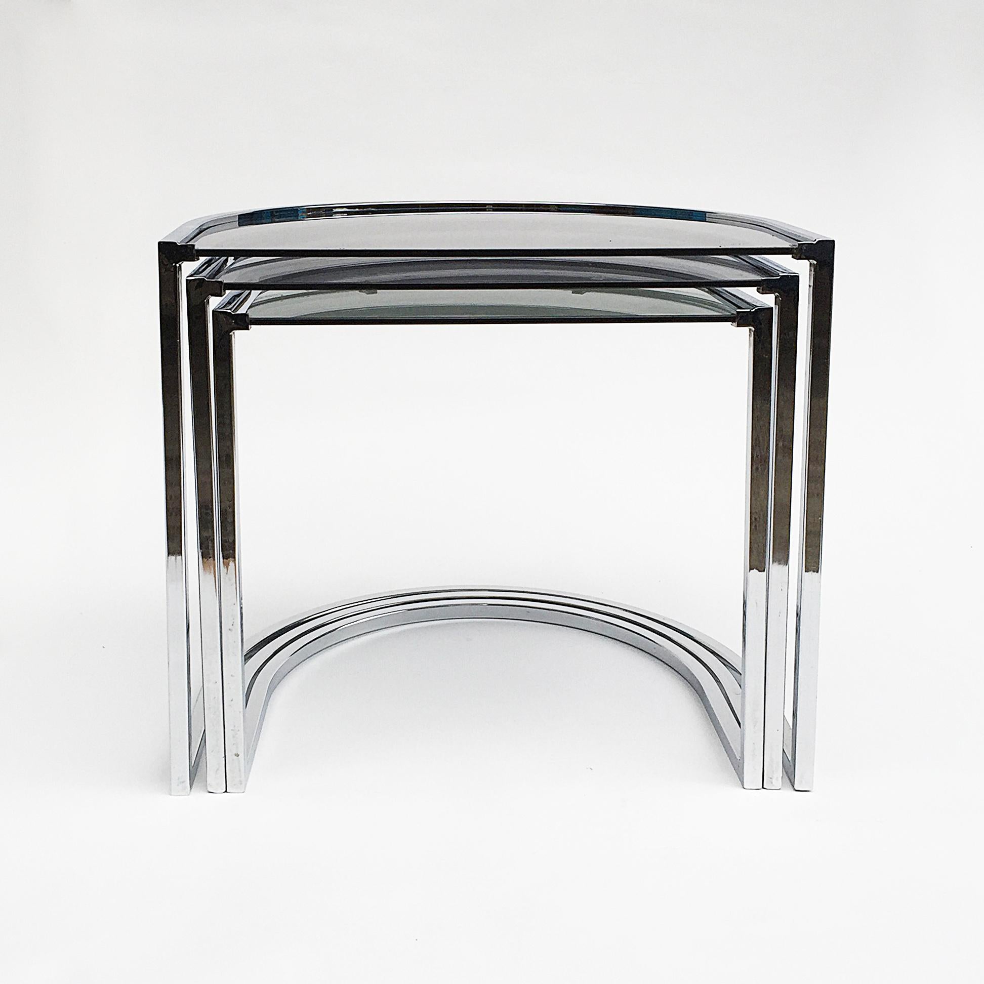 A minimal smoked glass top and chrome nest tables in the style of Milo Baughman. Curved elegant yet modern lines the two larger glass tops have darker glass than the lower small one. For an accurate international quote please message us.