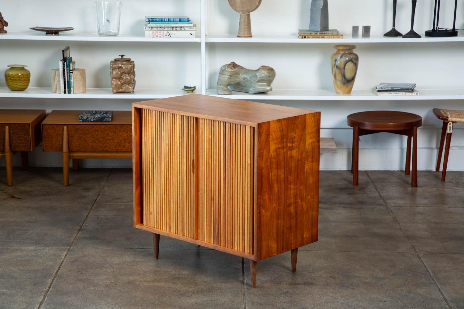 A Milo Baughman for Glenn of California tambour door cabinet. The cabinet features an oiled walnut frame and doors with a sliding walnut shelf atop three red painted drawers. We have two cabinets available and they are priced individually.