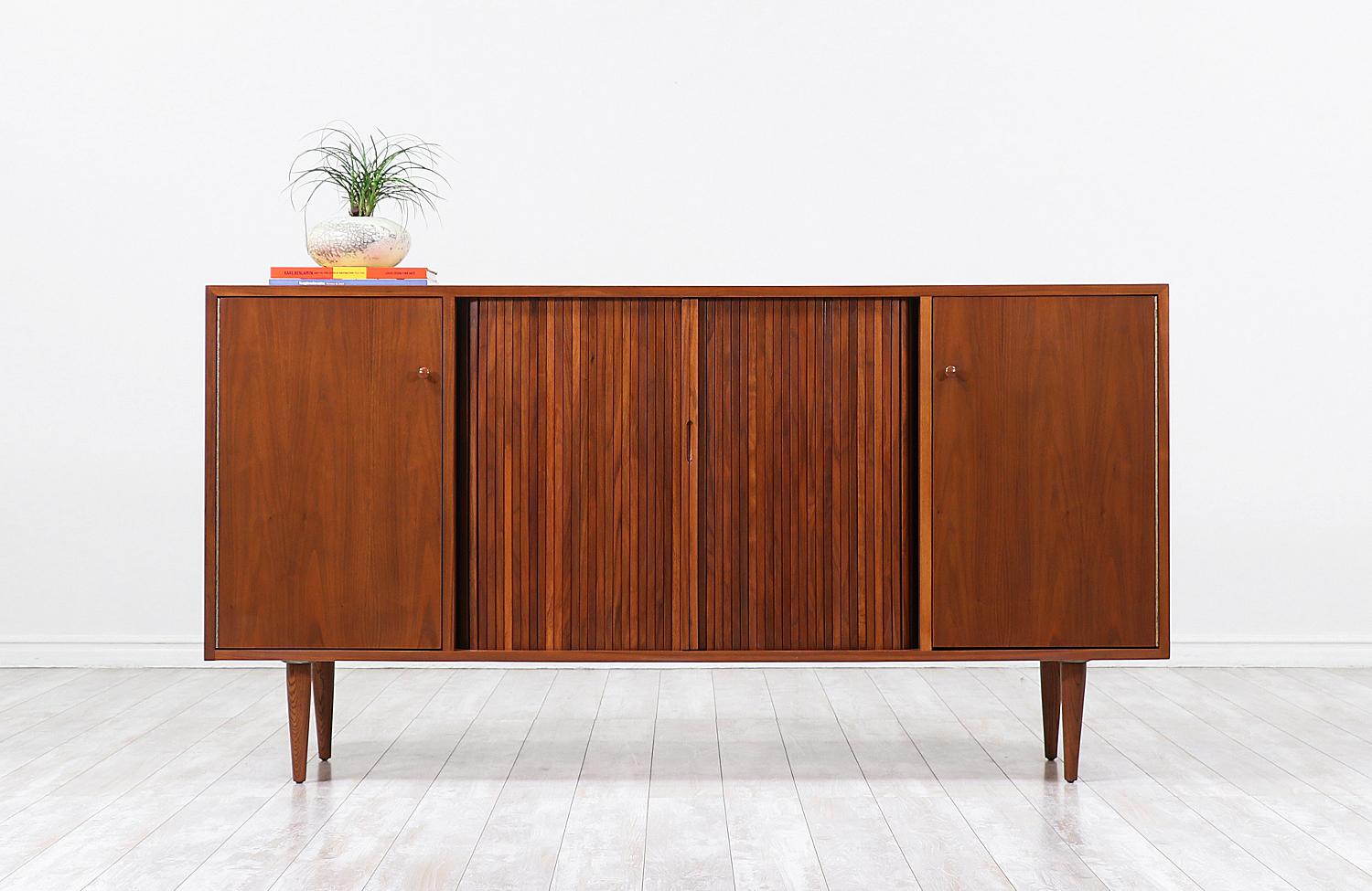 Mid-Century Modern credenza designed by Milo Baughman for Glenn of California in the United States circa 1950s. This exceptional credenza is crafted in walnut wood that features a closed shelved compartment on each side and a set of tambour doors