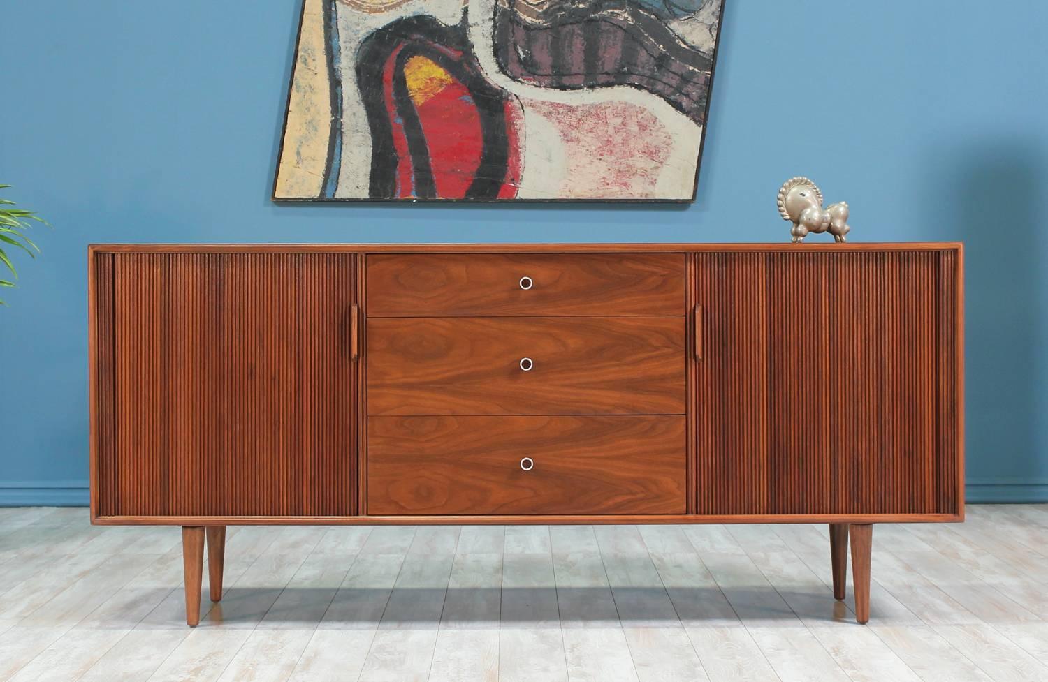 Tambour door credenza designed by Milo Baughman for Glenn of California in the United States circa 1960’s. This beautiful credenza features a walnut wood case, two tambour doors, one on each side, that open to reveal a shelved compartment. Three