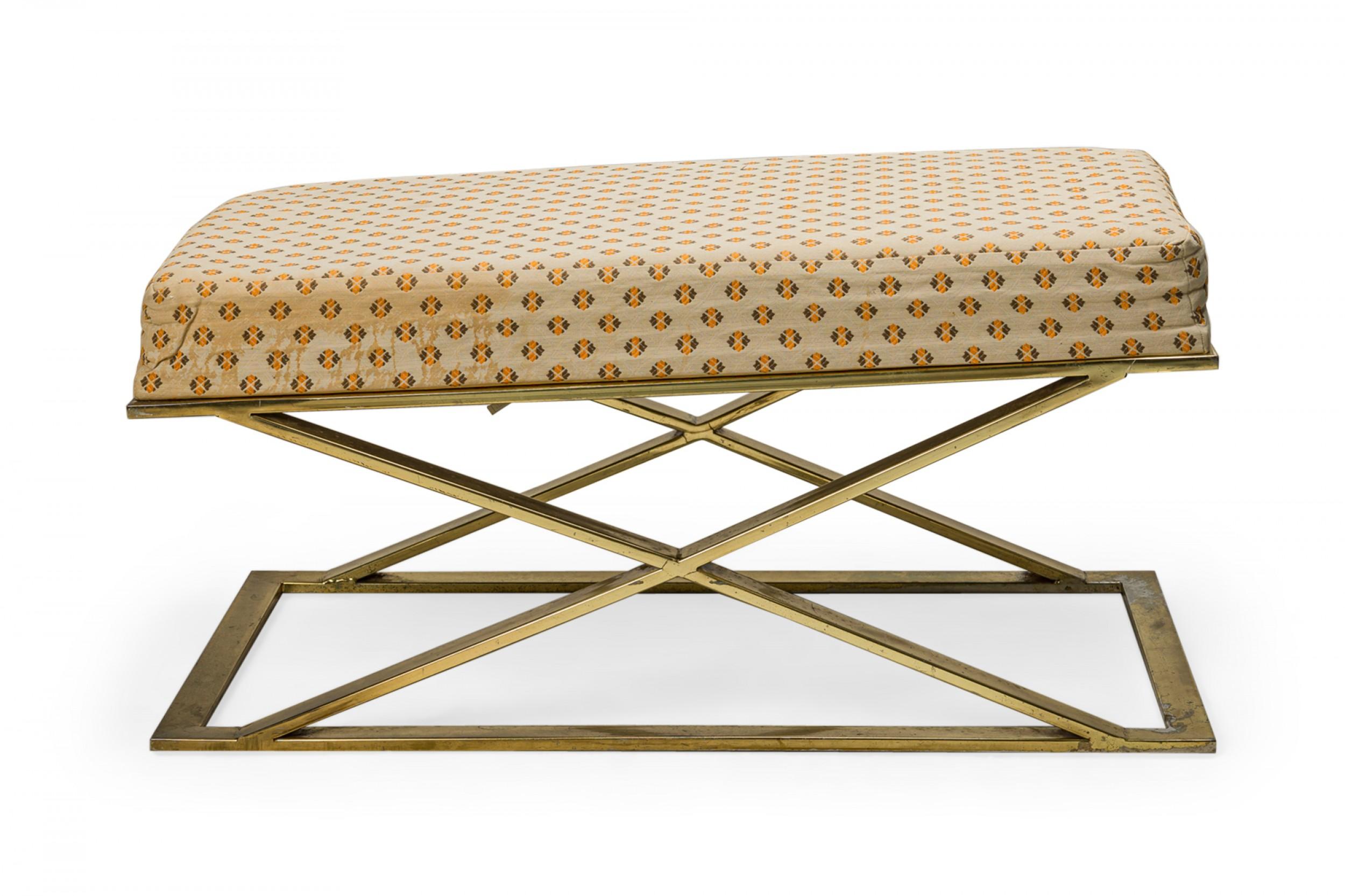 American Mid-Century bench with a beige, orange, and brown patterned fabric upholstered seat resting on a brass X-form base. (MILO BAUGHMAN / THAYER COGGIN)(Similar piece: DUF0372)