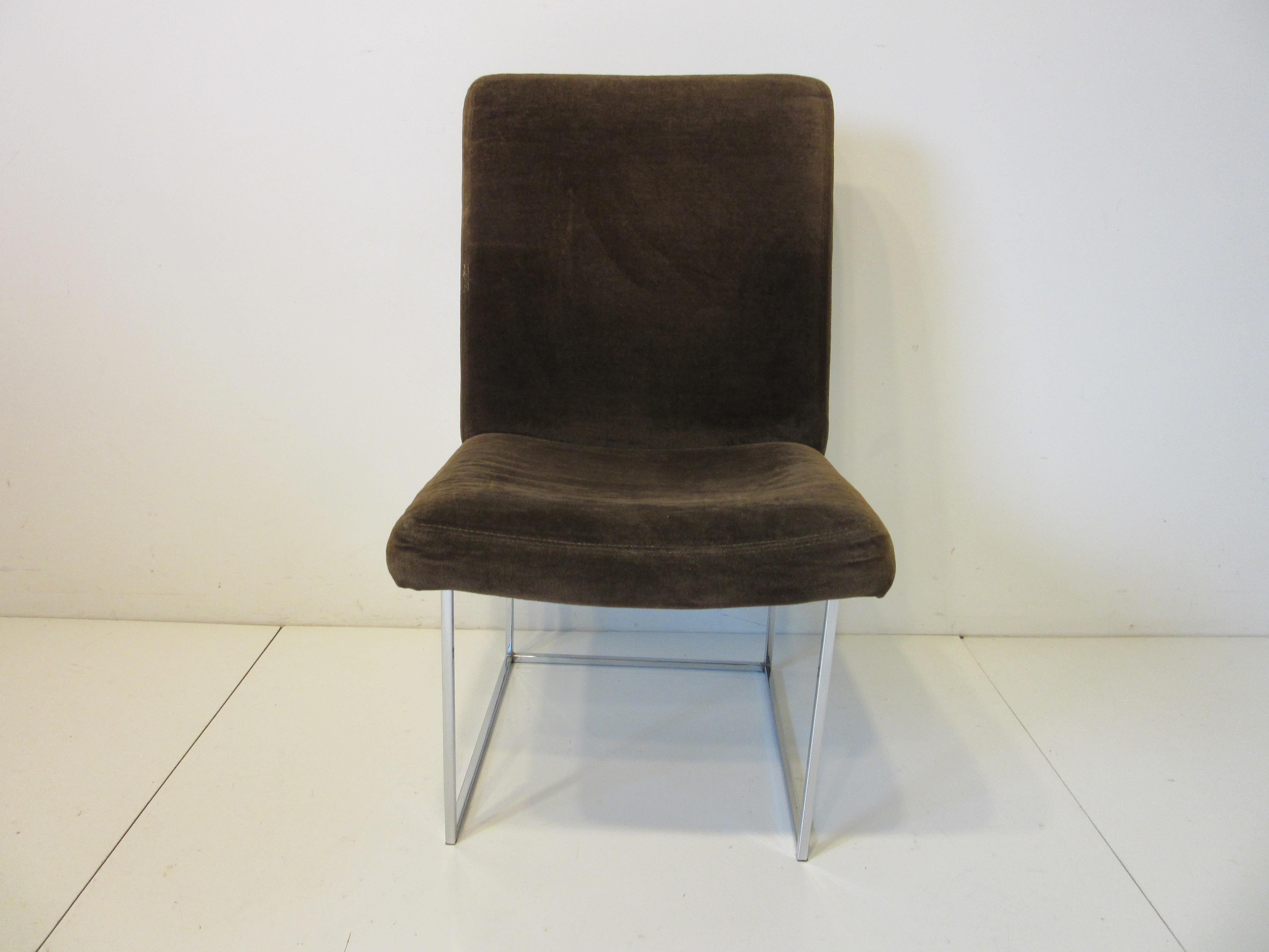 A set of four high back dining chairs upholstered in a dark chocolate brown velvet having chromed squared box tube framed bases. A comfortable chair that has a rich look and feel they still retain the manufactures labels and tags designed by Milo