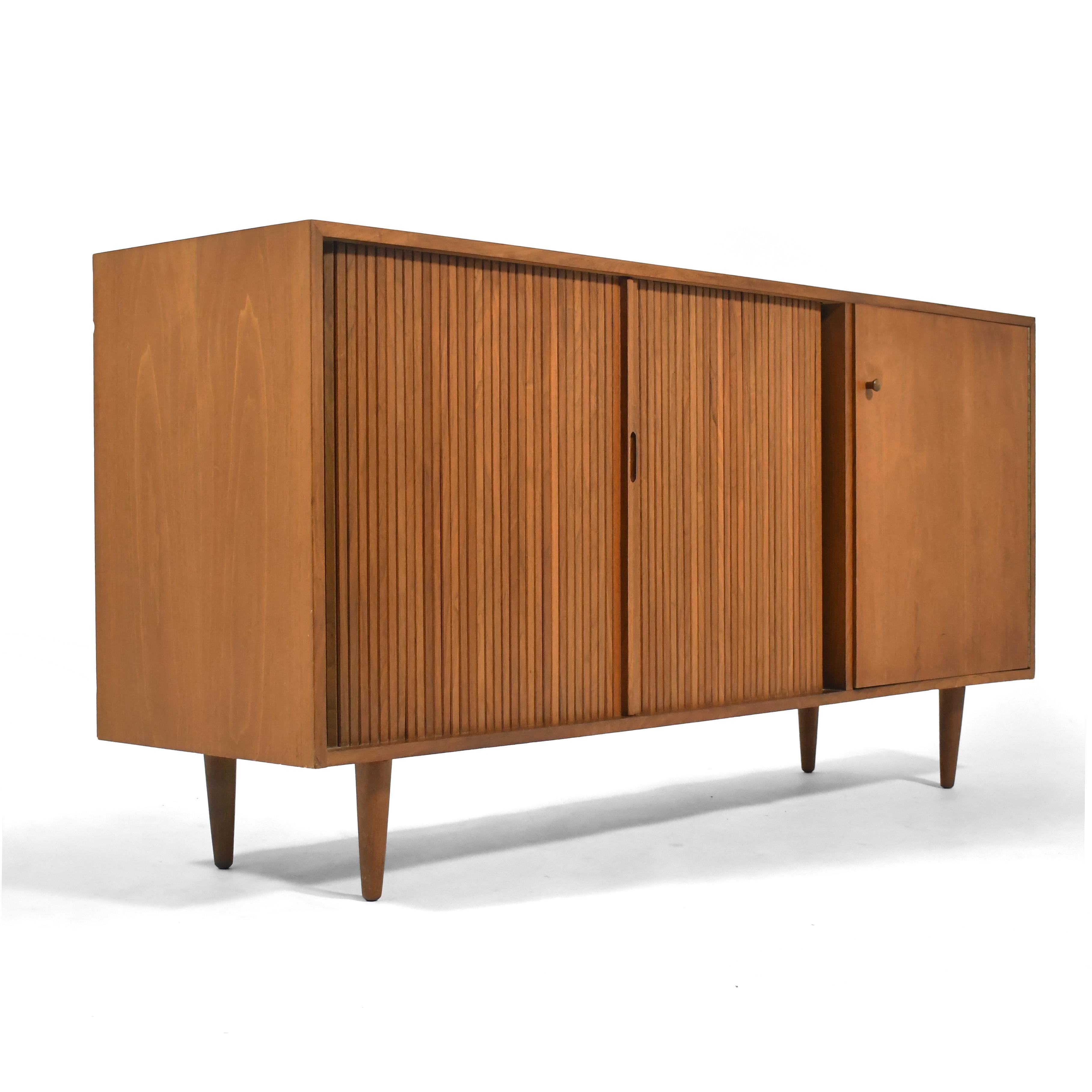 This walnut cabinet designed by Milo Baughman for Glenn of California is handsome and highly functional. The asymmetrical arrangement is very attractive. It has a single door which conceals a shallow drawer, a shelf, and two vertical storage