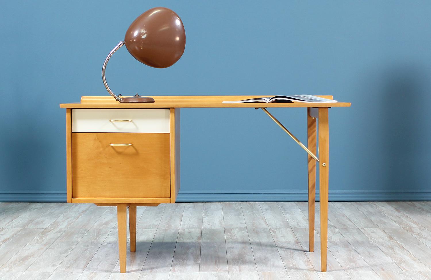 Gorgeous writing desk designed by Milo Baughman for Murray Furniture in the United States circa 1950’s. This lovely compact desk features a birch wood construction with brass hardware, which include the drawer pulls and the support rods underneath