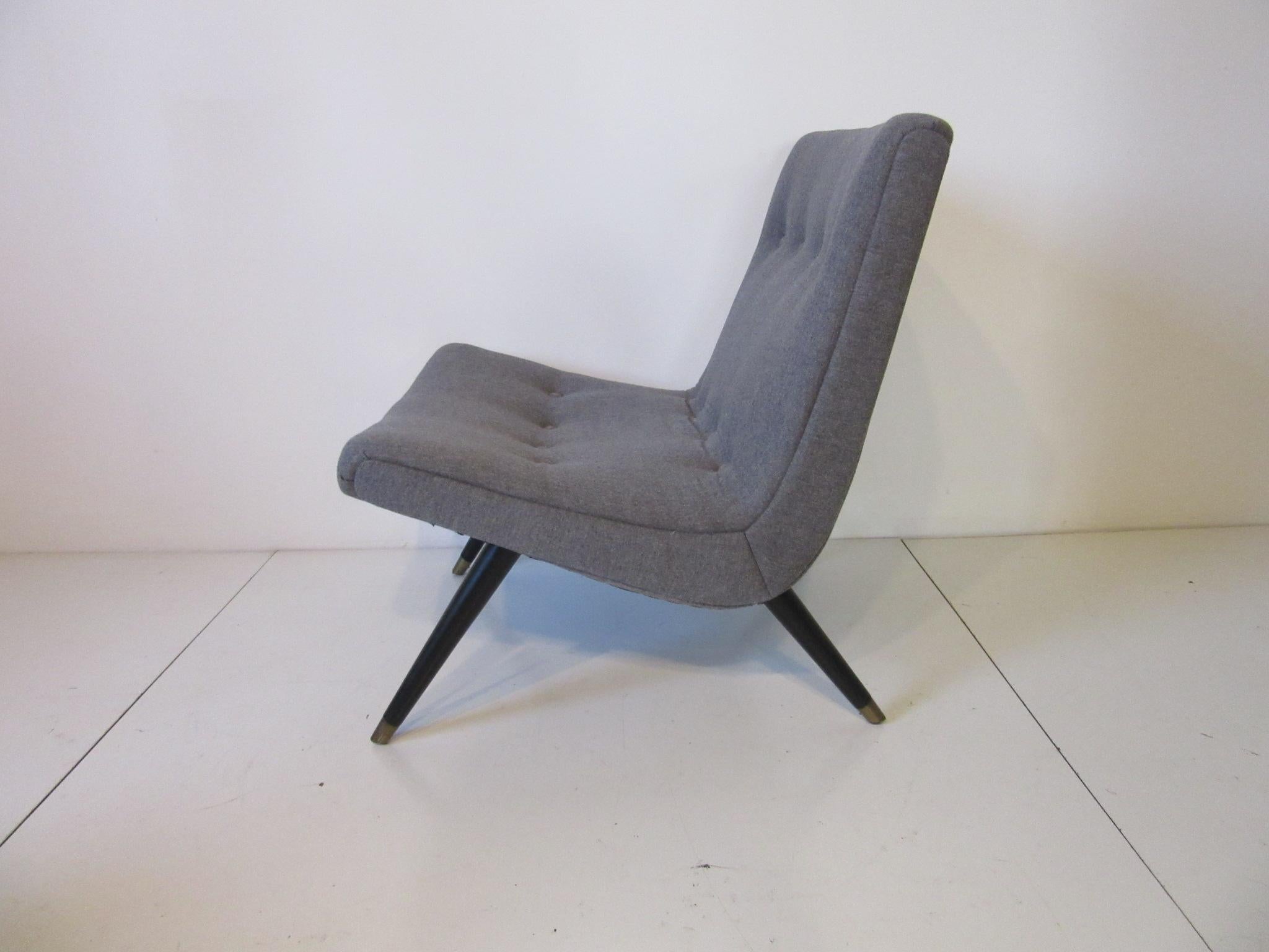 A gray flannel styled fabric upholstered scoop lounge chair and ottoman with button detail, satin black legs with brass capped feet a great compact size for that tight area . Measurement for the ottoman is 16