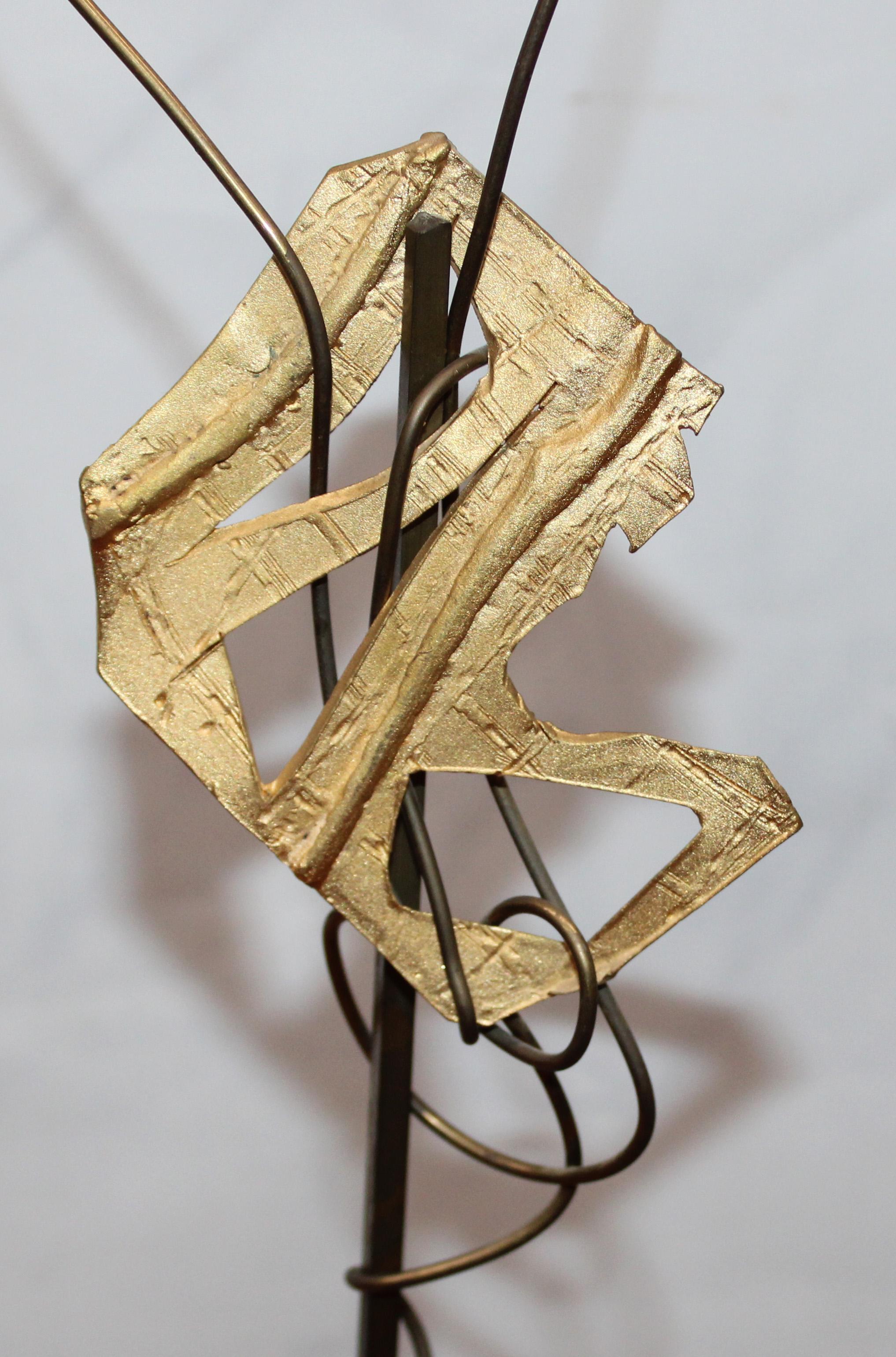 La escultura se compone de una base rectangular de madera, robusta y de acabado natural, sobre la que se erigen dos varillas metálicas verticales y delgadas. Una de las varillas sostiene una forma orgánica y translúcida, posiblemente de acrílico o