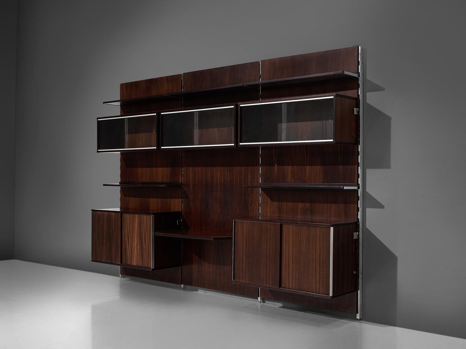 MIM Roma, cabinet, rosewood and metal, Italy, 1960s.

The monumental wall-mounted cabinet consists of four wall panels with various different storage facilities. The finish and details of this shelving wall unit are of a high standard. The piece