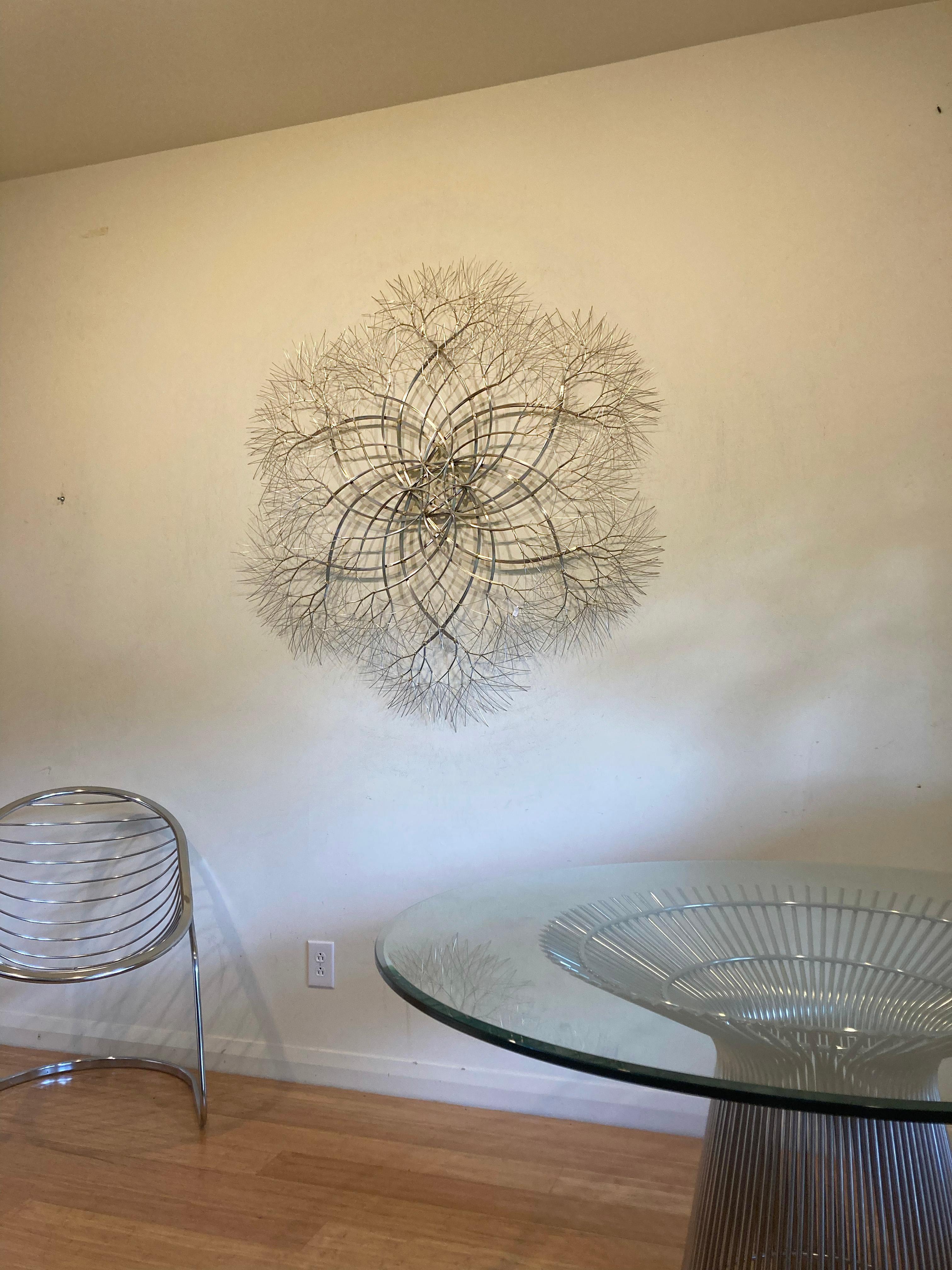 Stainless steel. 

This abstract wall art by Kue King is created using stainless steel wire. Kue uses an aesthetic reminiscent of trees, electricity, and light to create sculptures of peace and beauty. Adults and children alike see snowflakes,