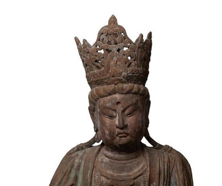 An imposing depiction of Guan Yin, wearing an elaborate headdress adored with the carved figure of the seated Amitabha Buddha, the face characteristically round and jeweled, with the full mouth forming a pout under a plump upper lip, the eyes