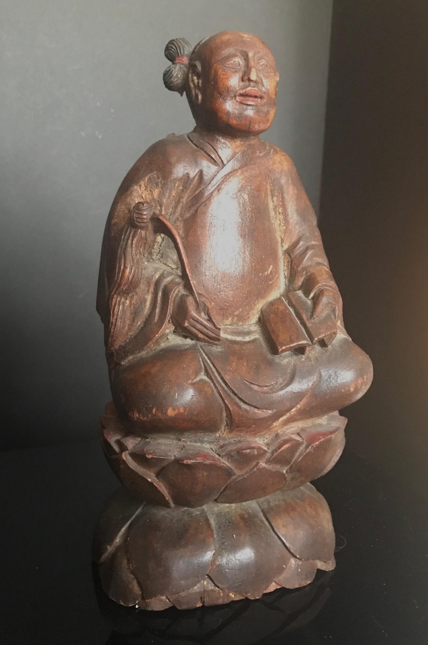 This is a rare and exquisite hand carved Daoist immortal figure. He is seated in a quiet meditation pose on a lotus flower. In his right hand he holds a finely carved fly whisk. His hair is pulled into two a double topknots. (One topknot is
