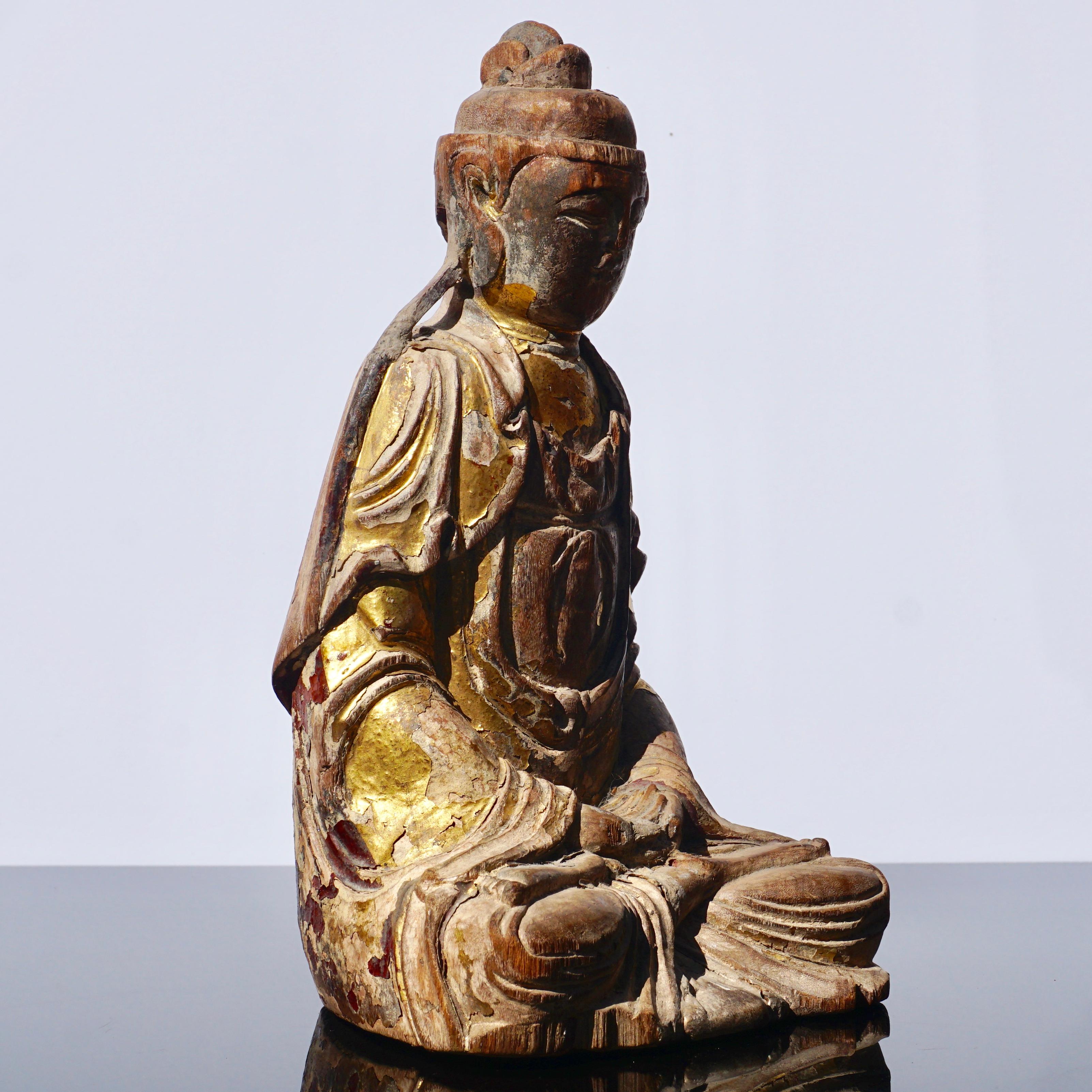 A beautifully carved wooden Buddhist spiritual figure with traces of gold gilded leaf. The seated Buddha statue is gazing down with hand clasped in his lap. Traces old ox blood polychrome on robe verso. Compartment for parlayed cutout on back seams