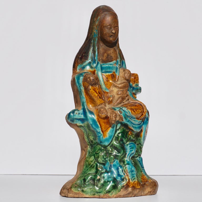 A Chinese Fahua glazed pottery figure of Songzi Guanyin with child. A rare yellow, turquoise and green glazed statue of Guanyin with downward gaze holding a baby on her left knee with right knee raised on an outcropping pedestal.

Very good