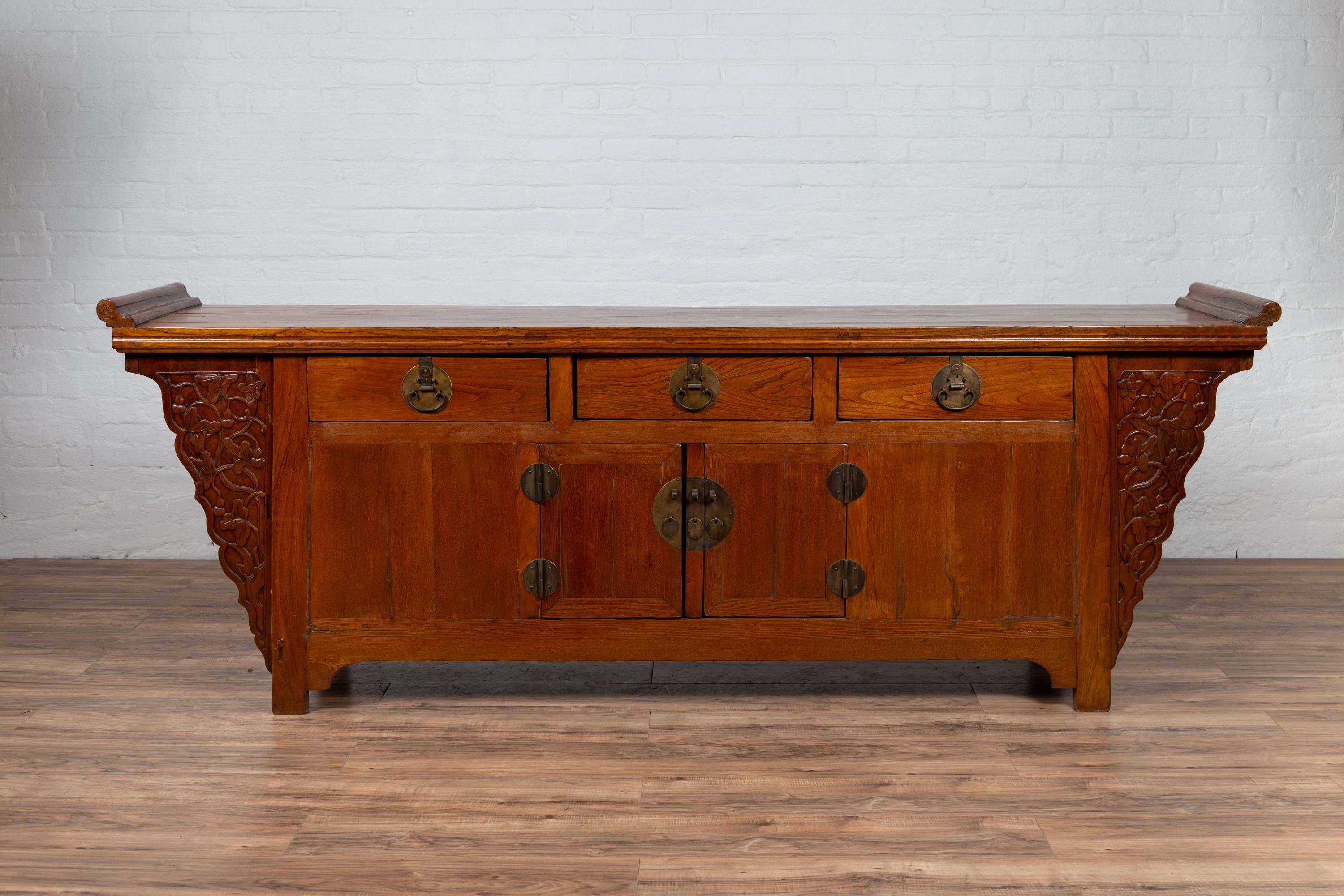 A large antique Chinese Ming dynasty style altar cabinet from the early 20th century, with everted flanges, three drawers over double doors and carved spandrels. Born in China during the early years of the 20th century, this exquisite sideboard