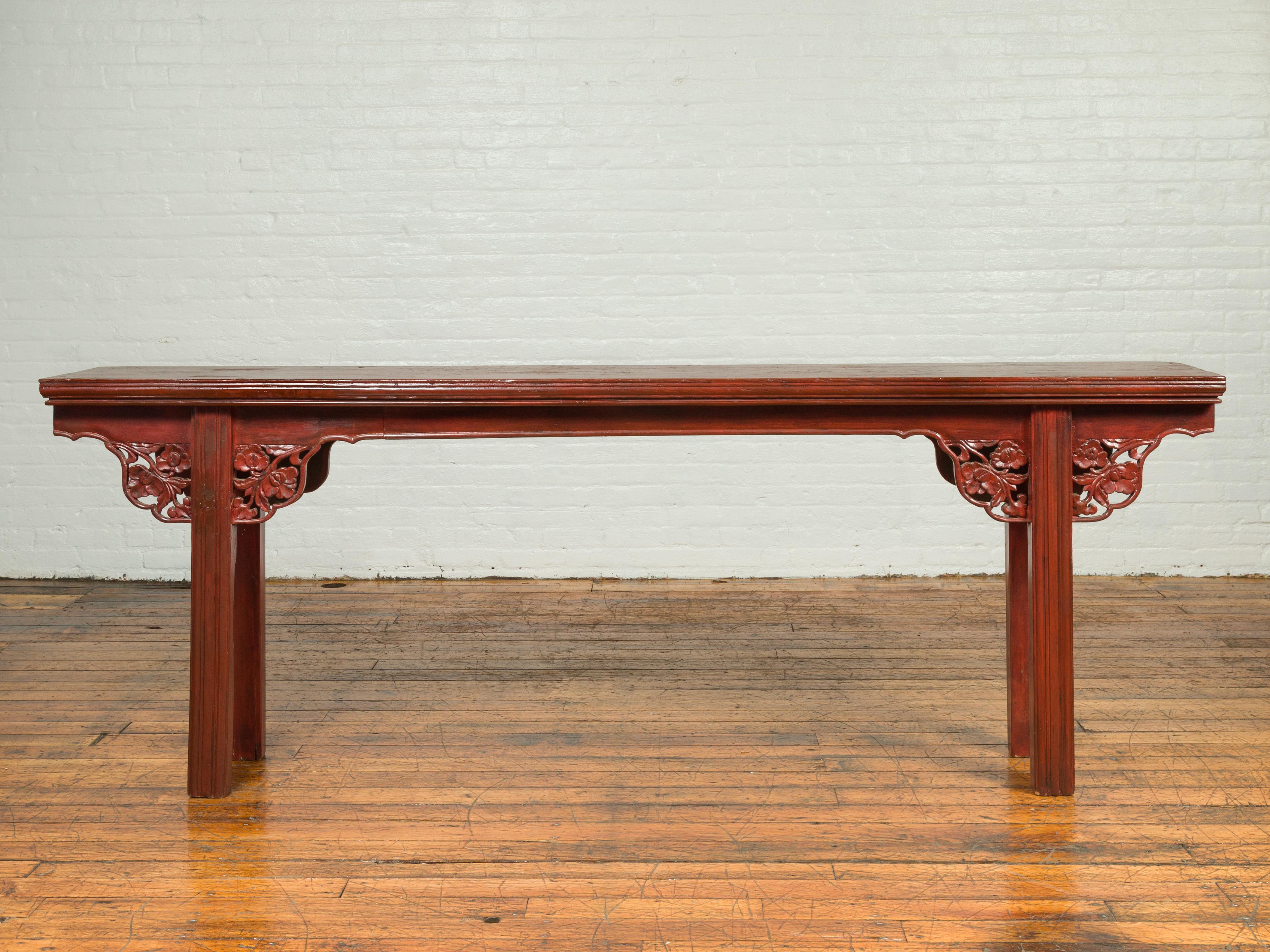 A Chinese Ming Dynasty style elm wood altar console table from the 19th century, with sang de bœuf patina and carved floral apron. Born in China during the 19th century, this exquisite altar console table features a dark red lacquered finish,