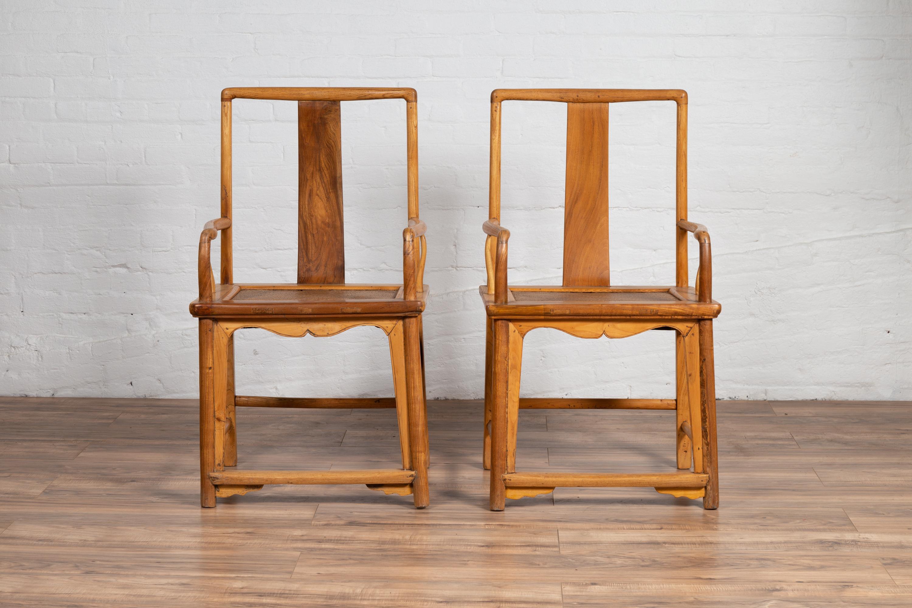 A near pair of Chinese Ming Dynasty style vintage wedding armchairs from the mid-20th century, with woven rattan seats, curving armrests and natural wood patina. Born in China during the mid-century period, each of this near pair (they present