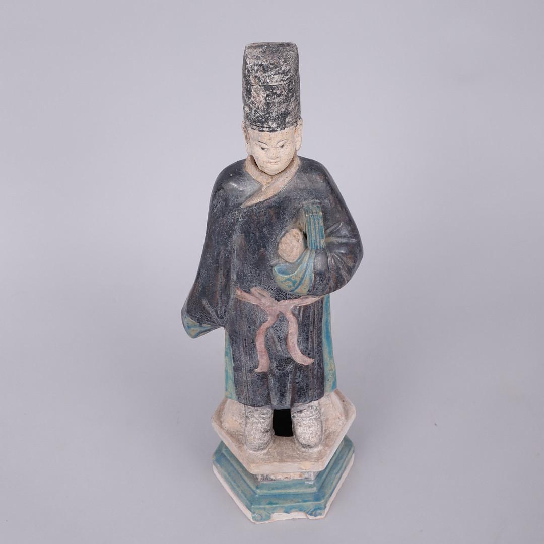 A fine green-glazed Chinese Ming Dynasty earthenware figure, depicting a official. The statue has been styled in long, flowing robes, colored in a vivid green. Additional features have been accented in a deep amber yellow. The head and the other