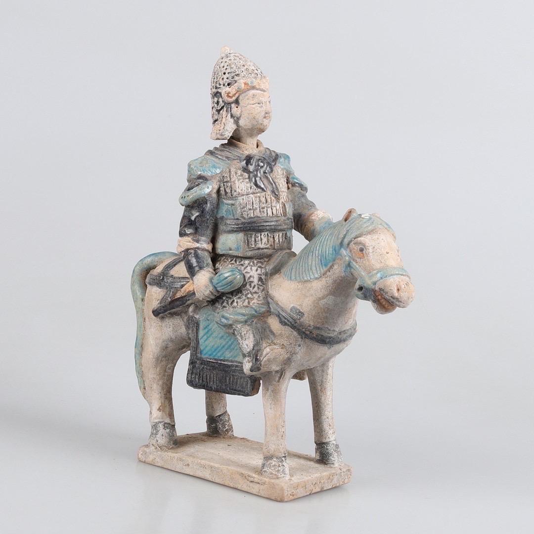 A fine green-glazed Chinese Ming Dynasty earthenware figure, depicting a knight or officer at horse. The statue has been styled in a war lord robe, with very detailed elements partly glazed in green, dark blue and yellow. The head and the other