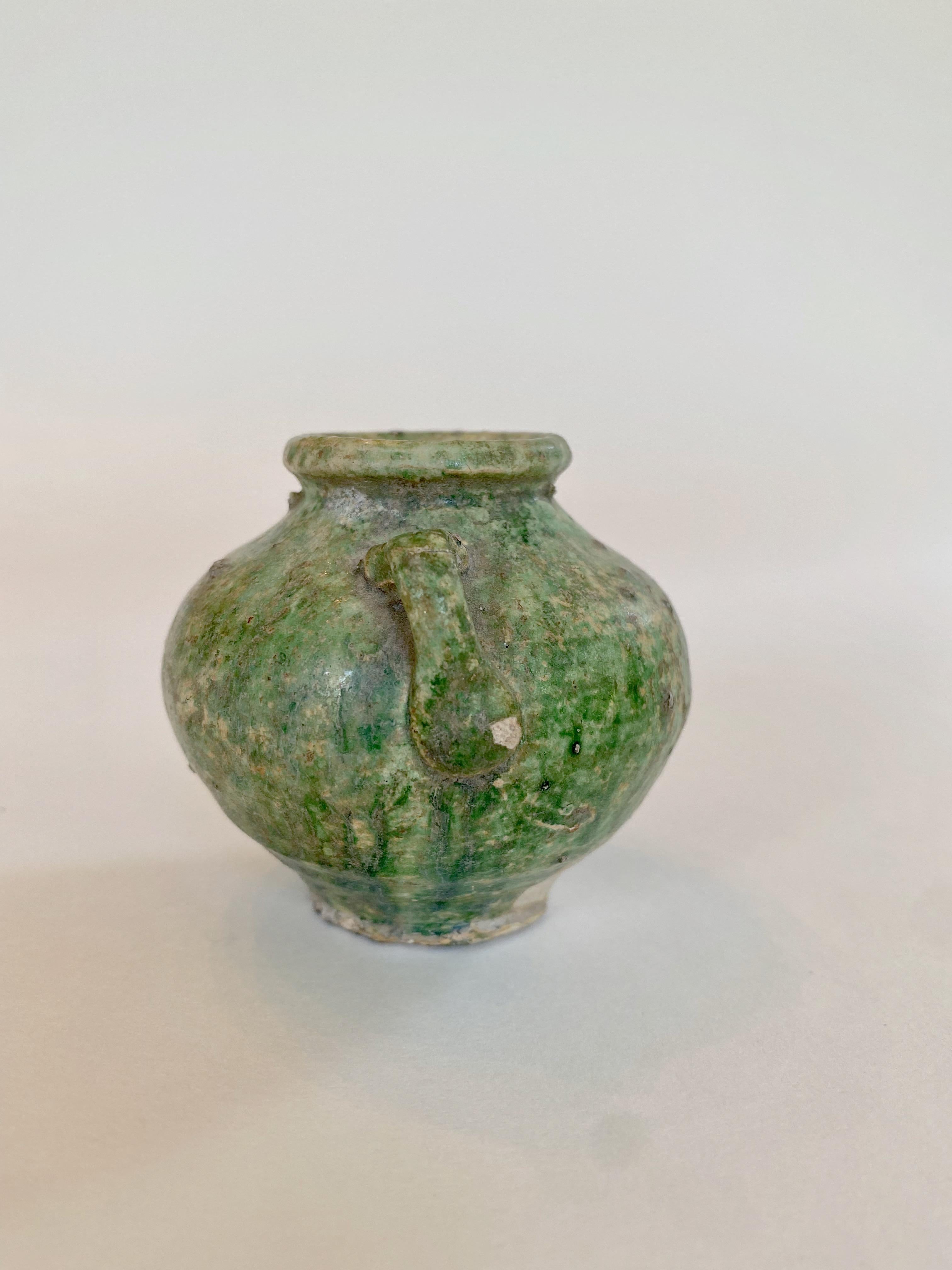 Small Ming pottery jarlet with handles and a green glaze. 16th century. 
This charming, somewhat rustic piece is like a miniature version of the large earthenware jars used to store water. It has a rounded body, small handles, and a pronounced lip.