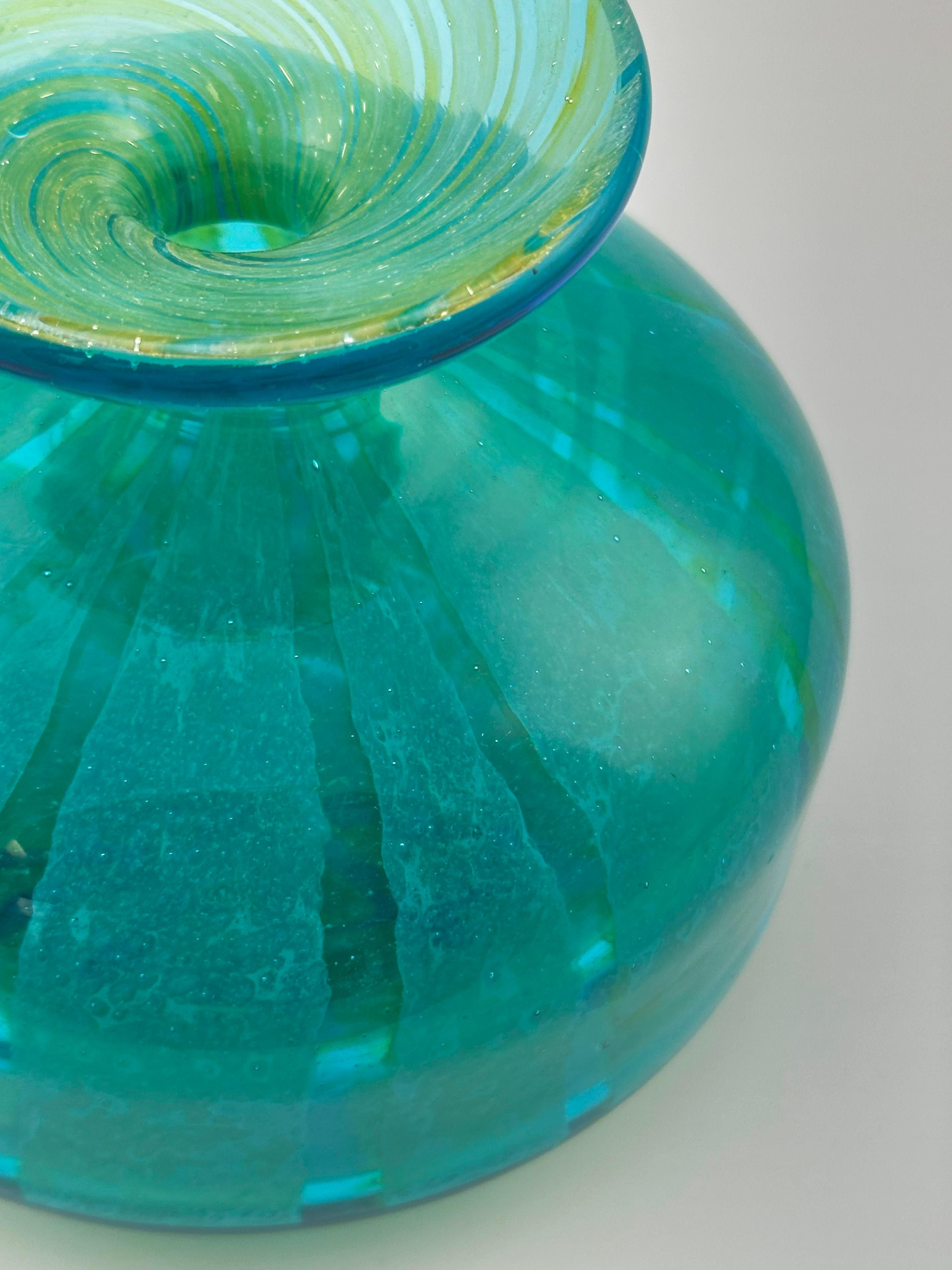 Ce vase en verre décoratif turquoise et vert est un bel exemple de l'art du verre maltais du milieu du siècle, fabriqué dans les années 1970 par le célèbre studio Mdina Glass. Formé en forme de bouteille trapue, il présente une base généreusement