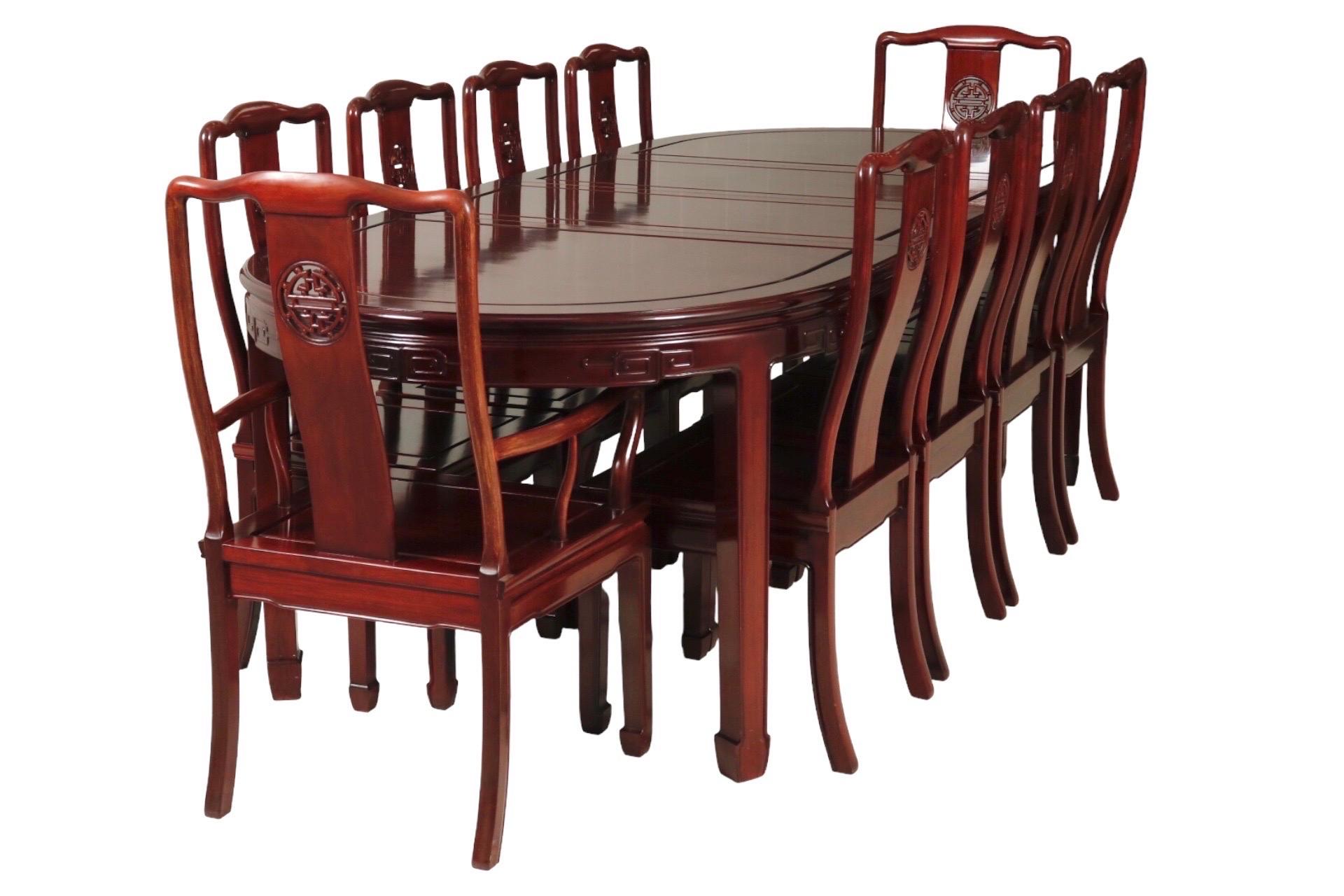 A Ming style dining table and ten chairs made of solid rosewood. The oval shaped table has beveled panels and is decorated with squared scrolls on the skirt. Extends with two leaves to comfortably seat ten, seats six without leaves. Two captain's