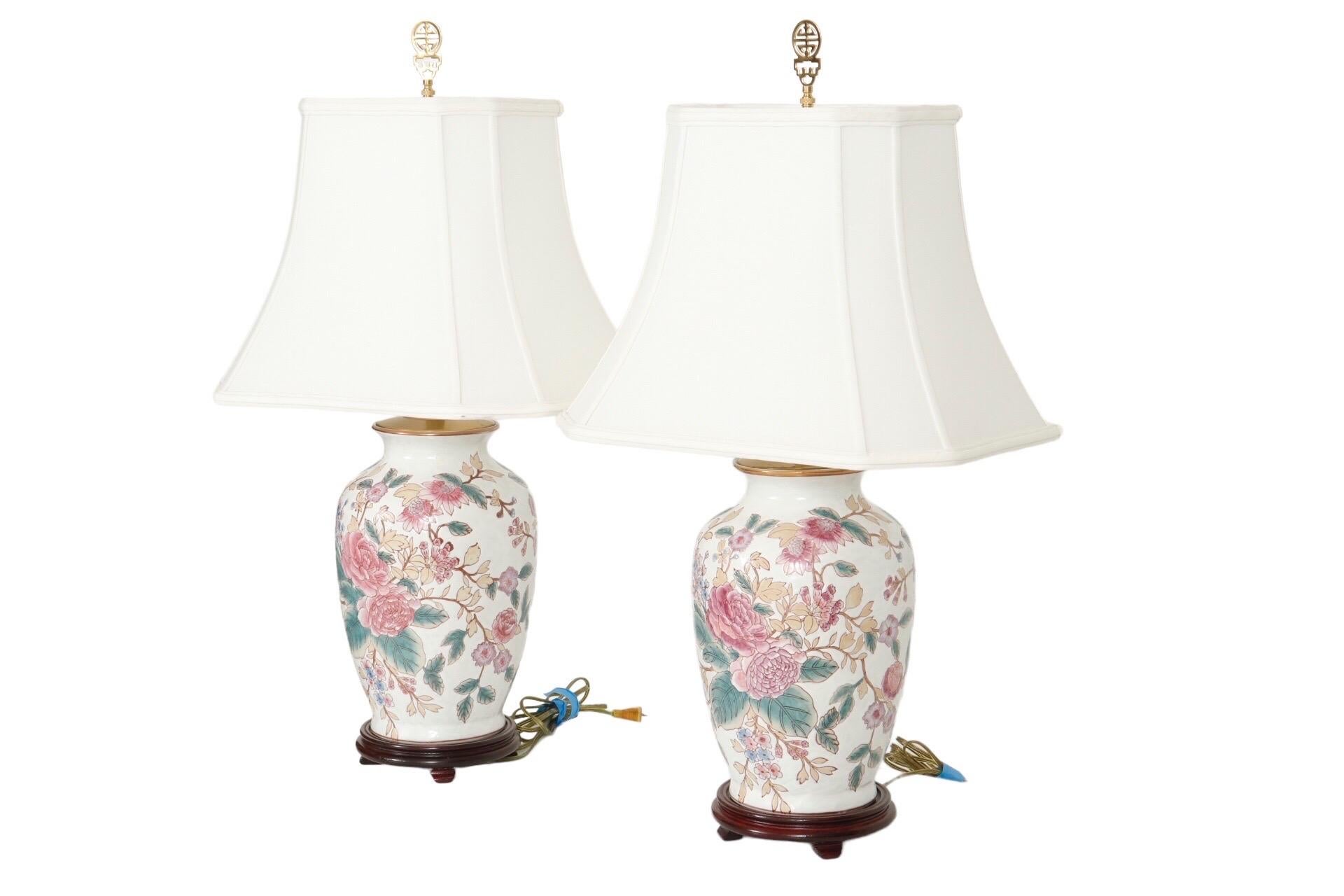 A pair of Ming style ceramic table lamps. Hand painted with subtle pink peonies, sprigs of crab apple flowers, and pale green and beige leaves on a white background. Crab apple flowers and peonies suggest the phrase 