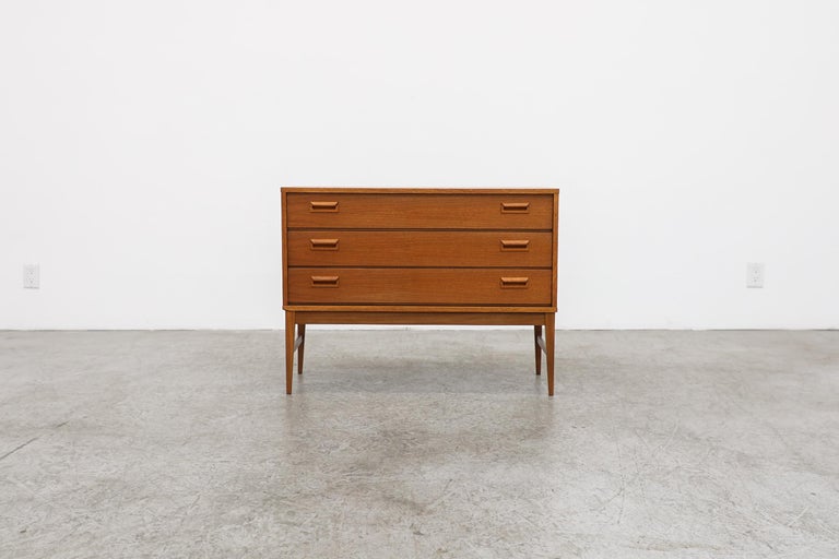 This Mid-Century Danish teak mini dresser or nightstand has 3 drawers with horizontal handles. In original condition with visible wear, consistent with its age and use.