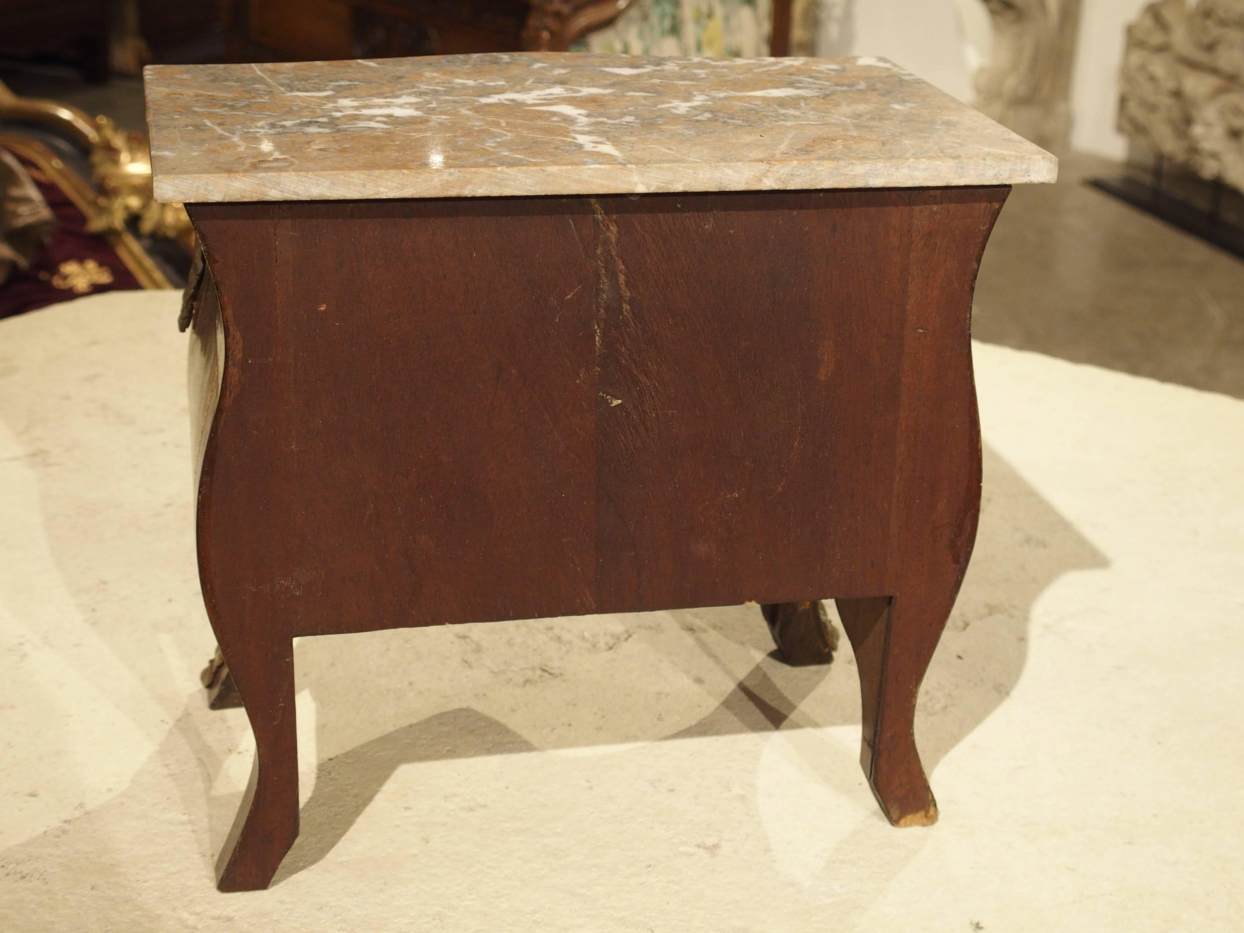 This antique miniature French tabletop commode with marble top dates to the 19th Century. It is in the Louis XV style with splayed feet, shaped (or 