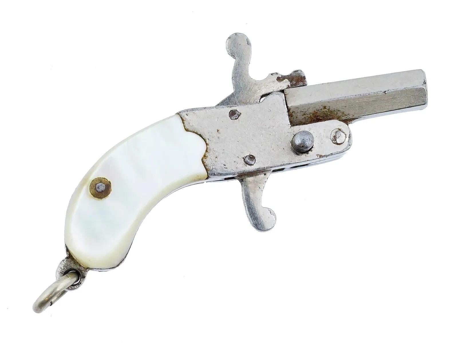 Un bibelot autrichien miniature en forme d'épingle. Le bibelot est réalisé dans un motif figuratif représentant un pistolet à feu. Nickelé avec poignées en nacre. Le canon porte un cachet autrichien sur le dessus. Bijoux et accessoires anciens et