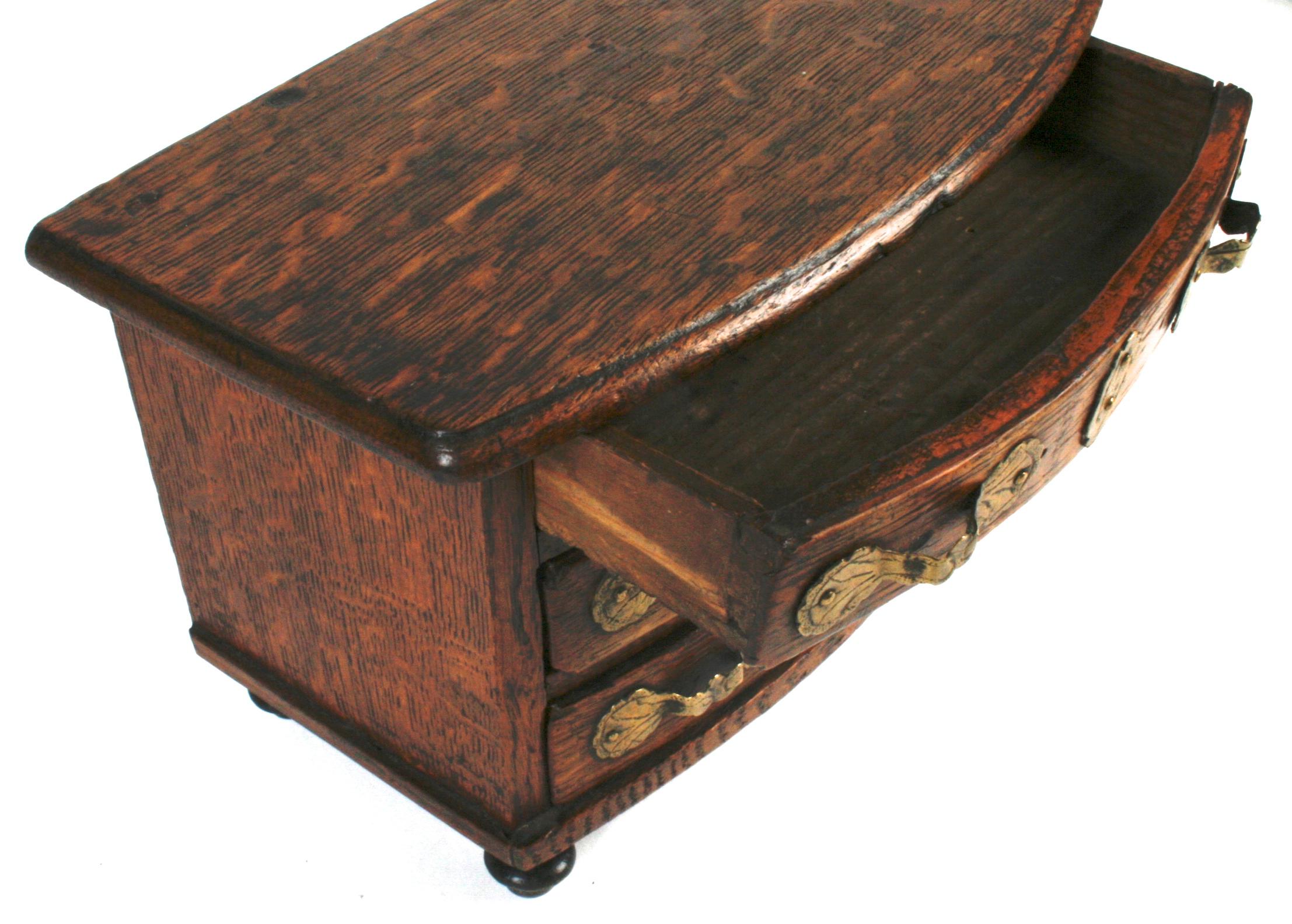 This handsome little oak chest has many of the same details of its larger counterparts. The bow fronted conforming top sits on three bowed drawers all with original brass pulls and escutcheons, and stands on small turned bun feet and engraved