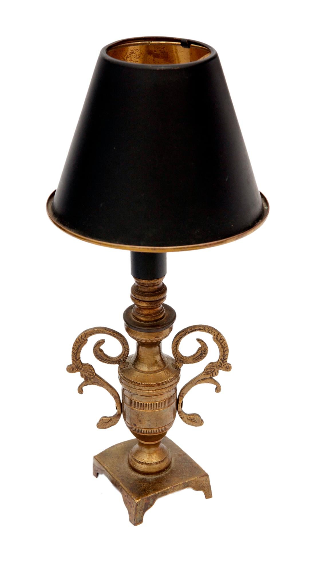 Petite night light/accent lamp in brass with a black metal shade included. The lamp has ornate arms, the shade has a rolled edge in brass. 
Takes a standard chandelier bulb. The switch is on the cord.