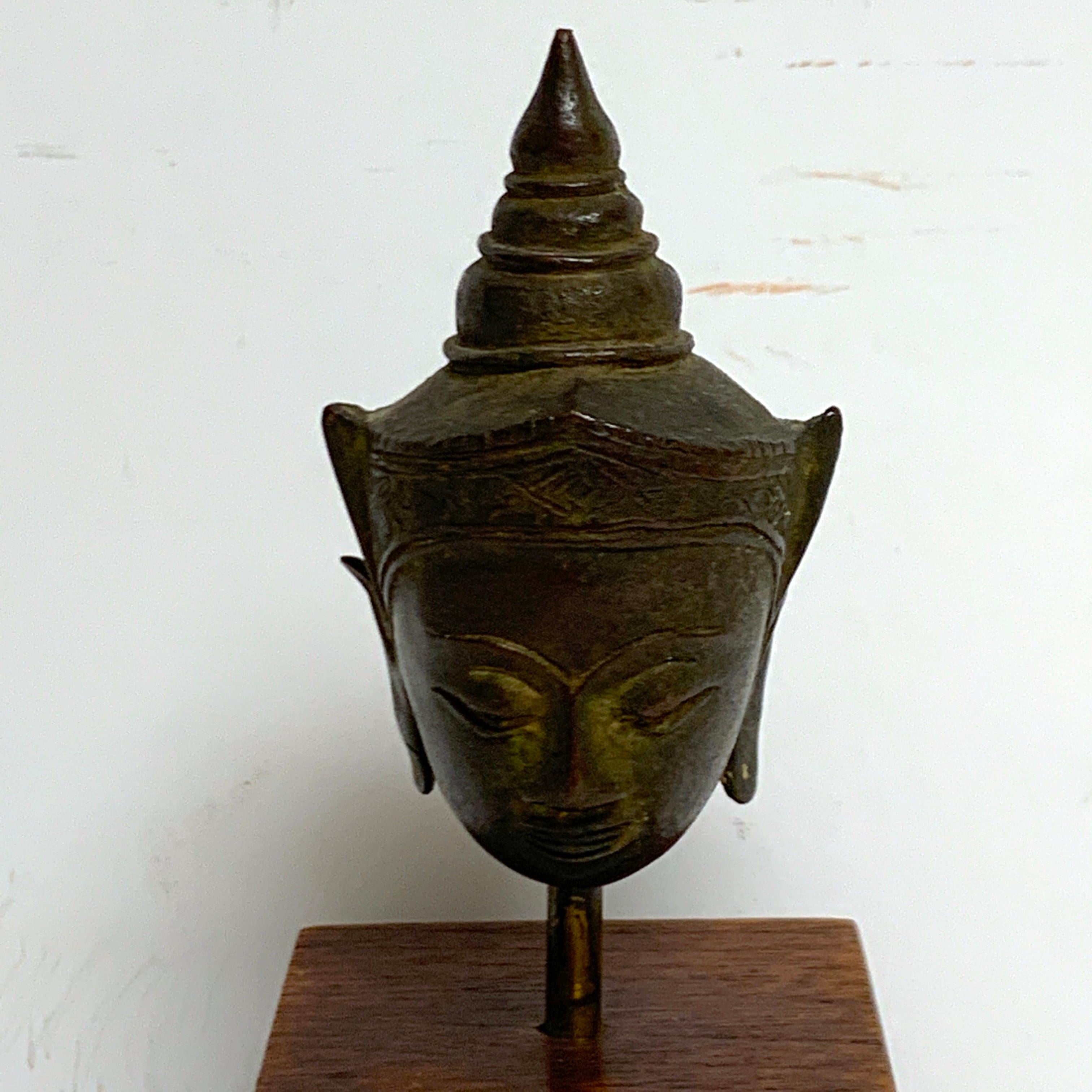 Miniature Bronze Thai Buddha Head, Museum mounted on a stepped wood pedestal. 20th century or older.
The sculpture alone measures 3