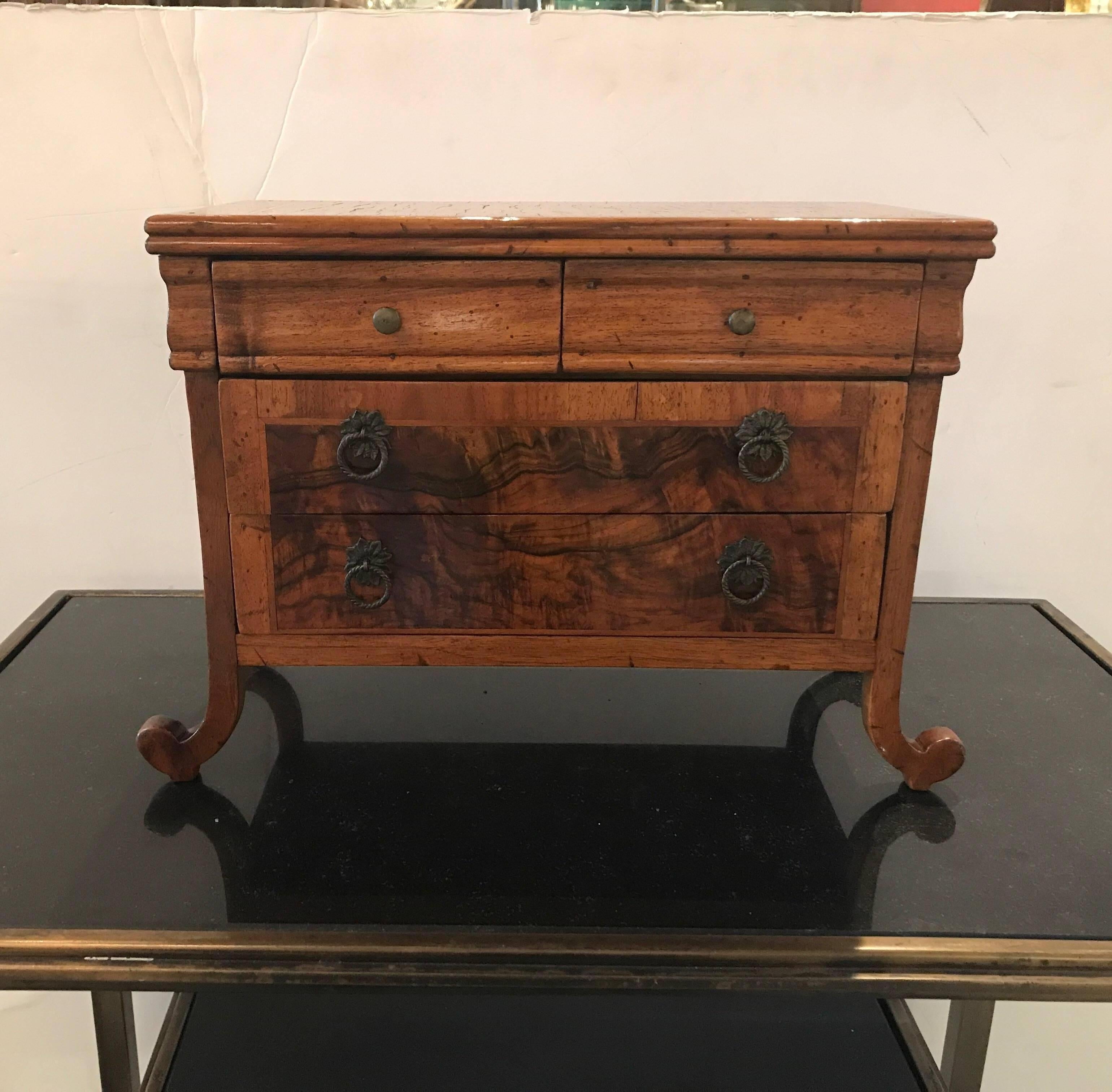 A handmade miniature chest of drawers with inlay. The walnut cabinet with burl wood inlaid panels. Two small drawers over two larger drawers resting on four scrolled and flared feet. The drawers have been relined in a simple red velvet.