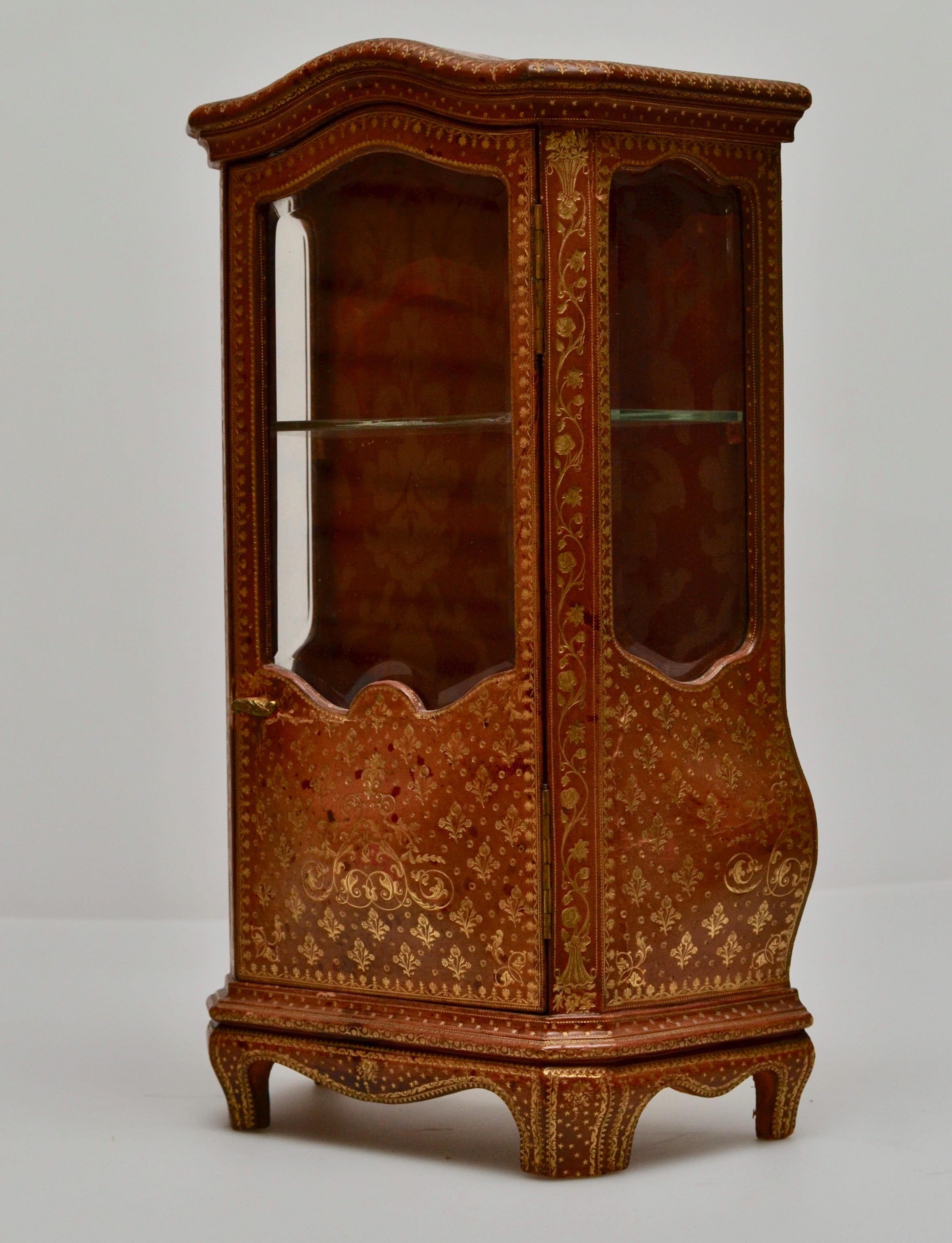 A miniature cabinet with gilt embossed leather, late 19th century-early 20th century. Wood frame.