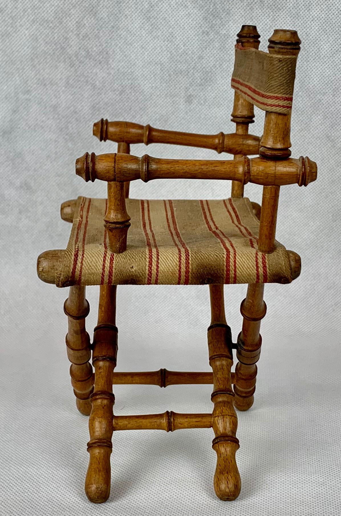 Miniature faux bamboo director's armchair carved from wood. The material with a green, red stripe on a natural ground is original. The chair was designed to fold, as the larger versions do.  This chair might have been created as a salesman's sample.