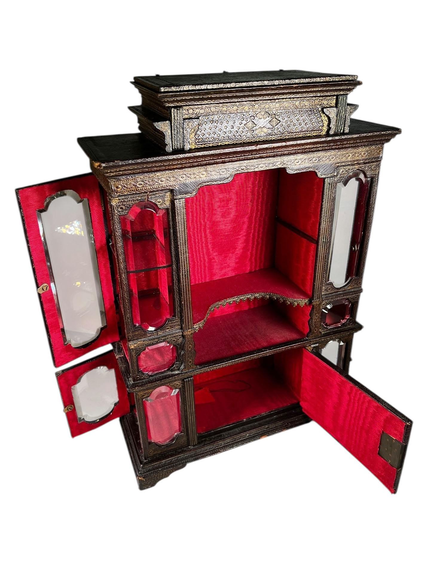 Ein seltener und fein gearbeiteter Miniaturschrank aus Florenz, CIRCA 1890, mit reich geprägtem Leder verkleidet und mit feiner Goldgravur versehen. Abgeschrägte Glasscheiben umrahmen alle Seiten und ermöglichen eine elegante Präsentation. Eine