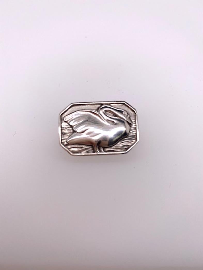 Petite sterling silver pin.  Made, signed and numbered by GEORG JENSEN.  Rectangular octagonal shape, depicting an applied figural 