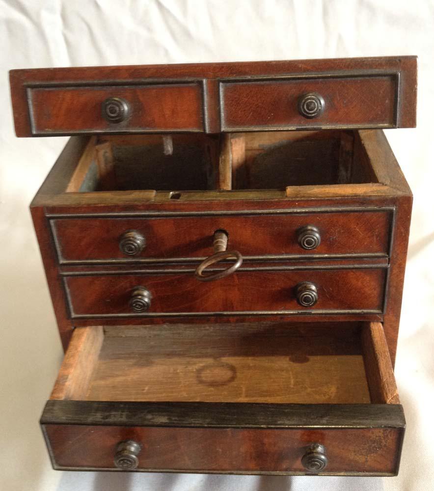 A miniature Georgian mahogany chest of drawers tea caddy with two short over three graduated long drawers, with shaped apron and on bracket feet. The top two drawers are hinged and open to reveal two wooden lidded tea containers, whilst the bottom
