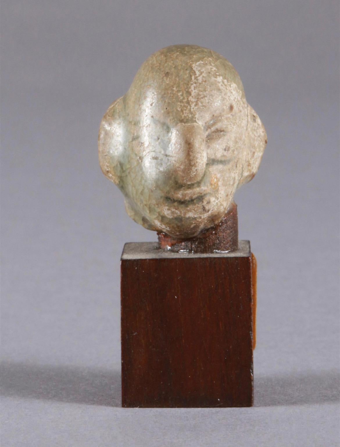 Miniature head made of ceramics on wooden base,, Cambodia, 20th century.

Provenance: Swiss private collection.

Additional information: 
Material: ceramics on wooden base.
Dimensions: H 2.5 cm.