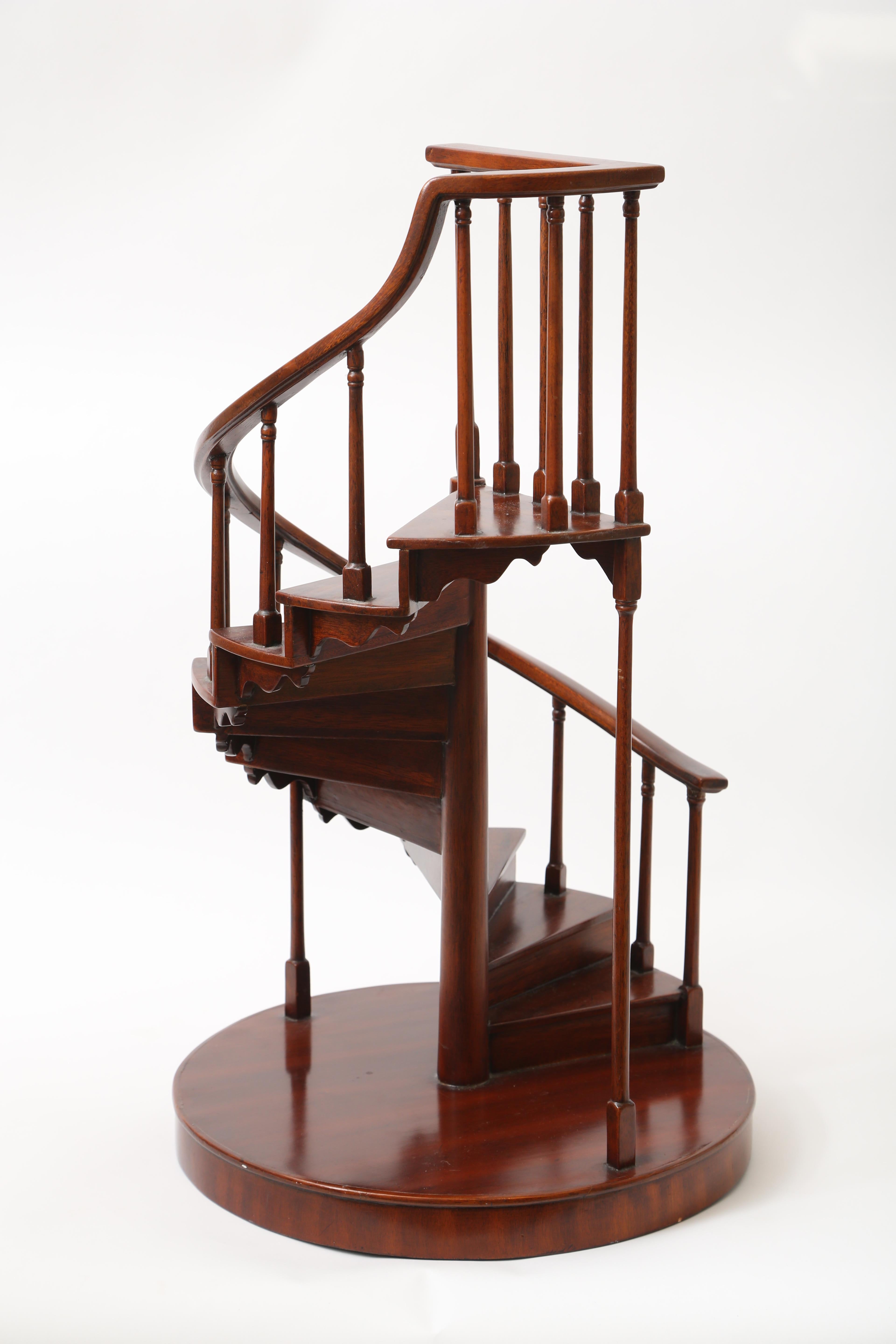 A Classic mahogany spiral staircase design with numerous small steps and turned baluster supports to the elegant curving railing, on a round base. Original sticker for Maitland Smith, an American manufacturer and seller of high quality decorative