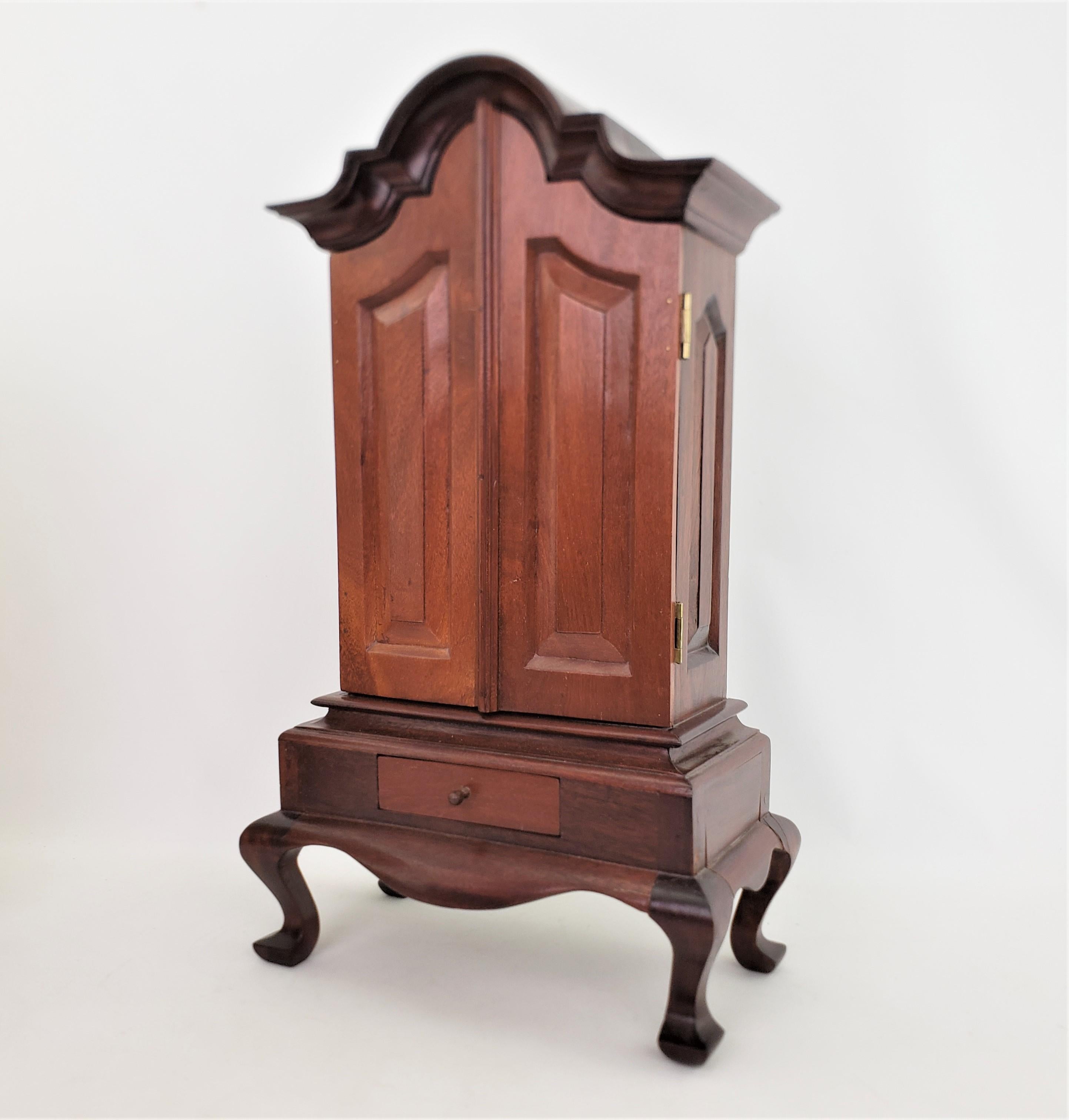 This very well executed miniature wooden cabinet it unsigned, but presumed to have originated from England and date to approximately 1940 and done in a Queen Anne style. The cupboard is made of solid walnut and has an elaborate serpentine top and