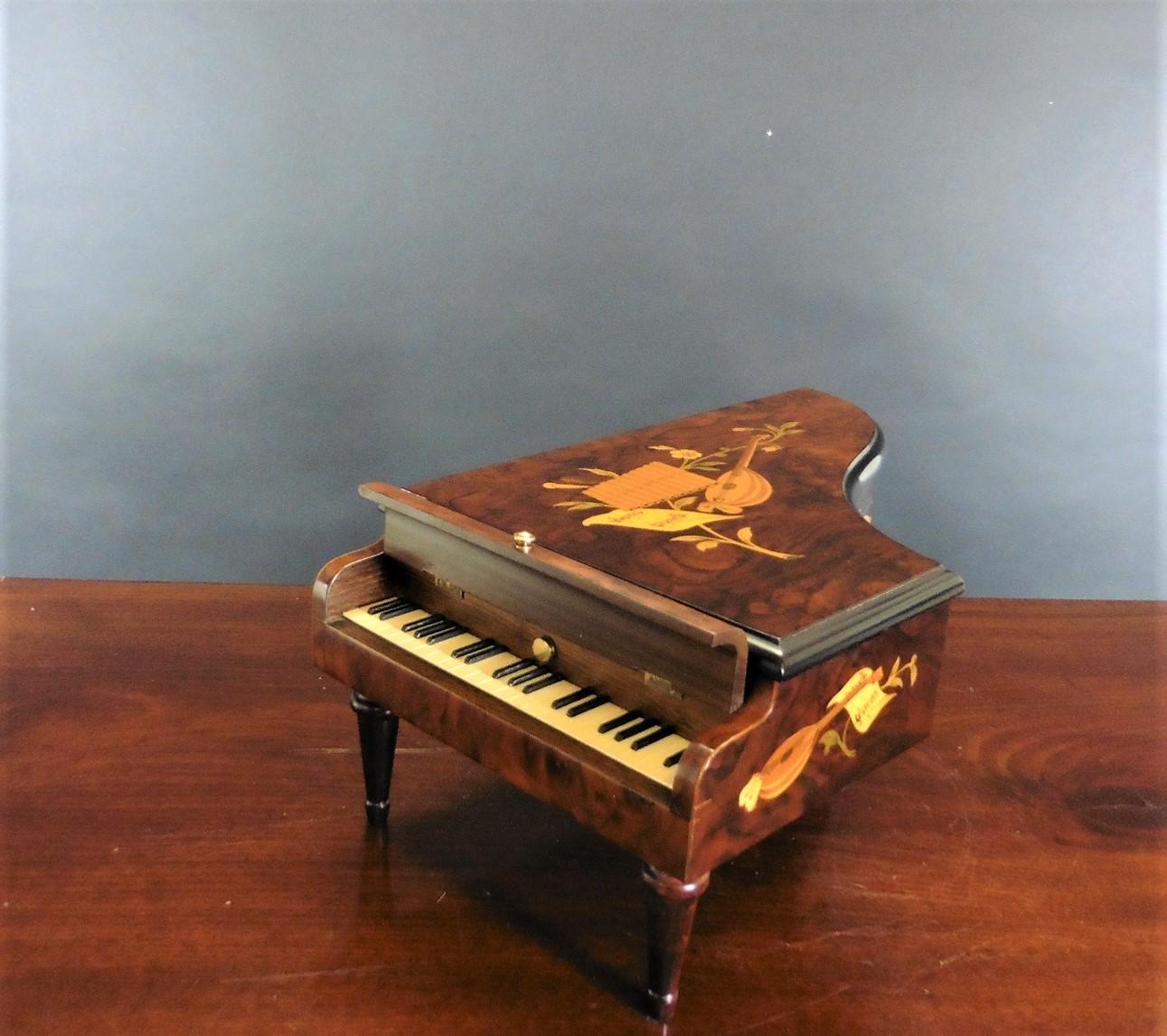 Music and jewelery box, Asprey London.
Movement by Reuge, Switzerland.

Miniature jewellery and music box in the style of a grand piano in a mahogany and walnut veneered case inlaid with marquetry throughout featuring musical instruments, raised