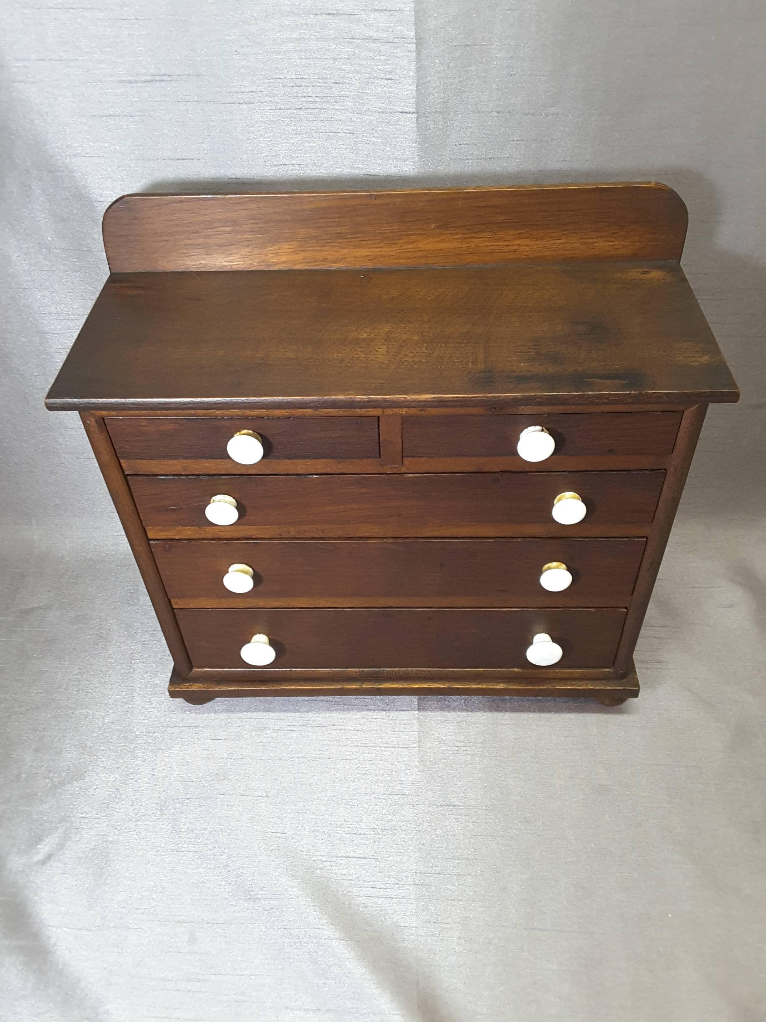 Miniature oak bonnet chest, five drawers, circa 1900, possibly a salesman's sample or children's toy. The case is done in oak with pine interior drawers and porcelain knobs. There is a small upper backboard, the case has four ball feet. The bonnet