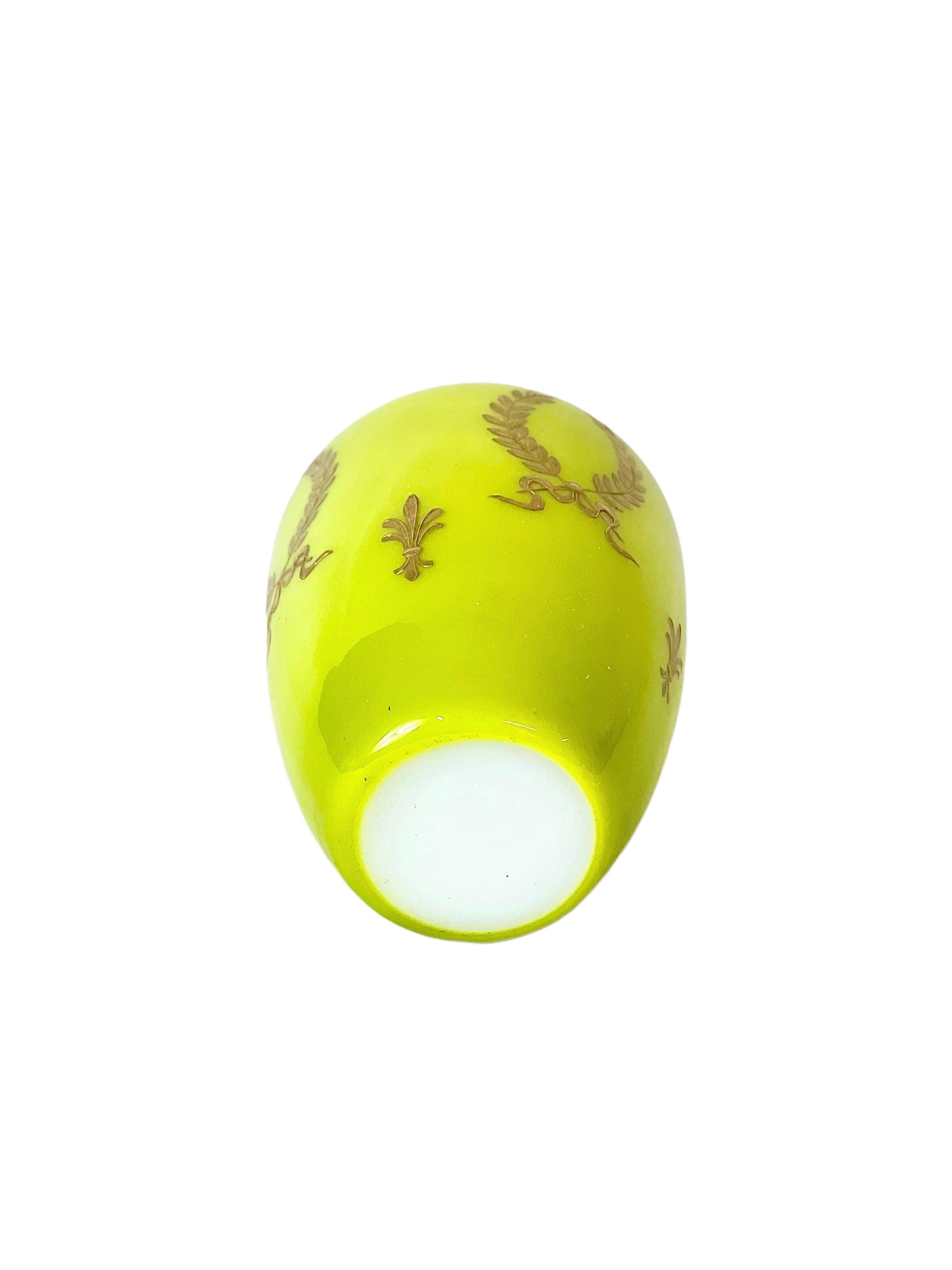 A charming, miniature opaline glass vase in a vibrant Chartreuse yellow, and decorated all around with stylised gilded laurel wreaths and fleurs-de-lys. This petite urn-shaped vase is pure white inside and has a delicately painted gilt rim to match