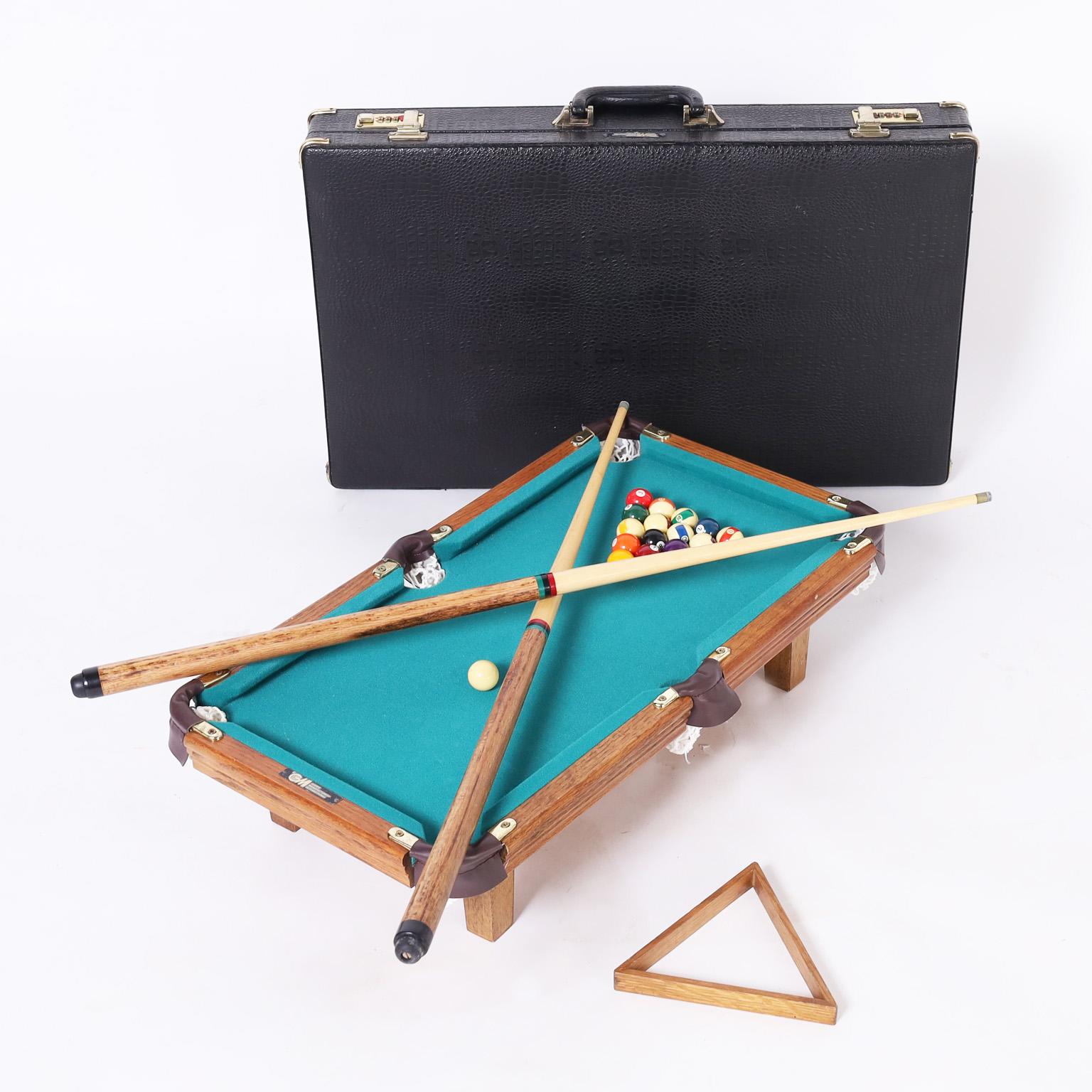 Vintage miniature pool table complete with cue ball, two cue sticks, fifteen numbered balls, lint brush, rack and faux lizard carrying case.