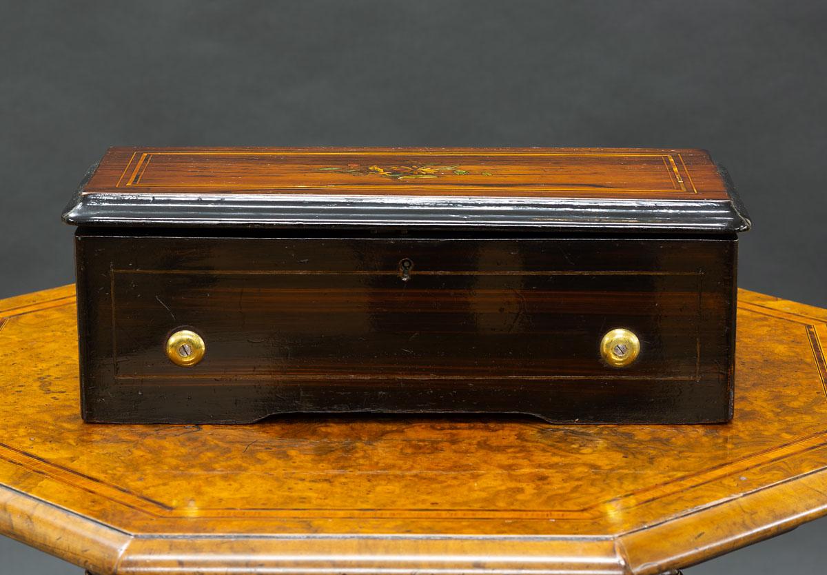 Swiss music box, circa 1890.



Rosewood miniature case with satinwood line stringing, the top decorated with beautiful inlay.

The hinged cover opening to a glazed top revealing the jewelled movement with winding handle and bar damper,