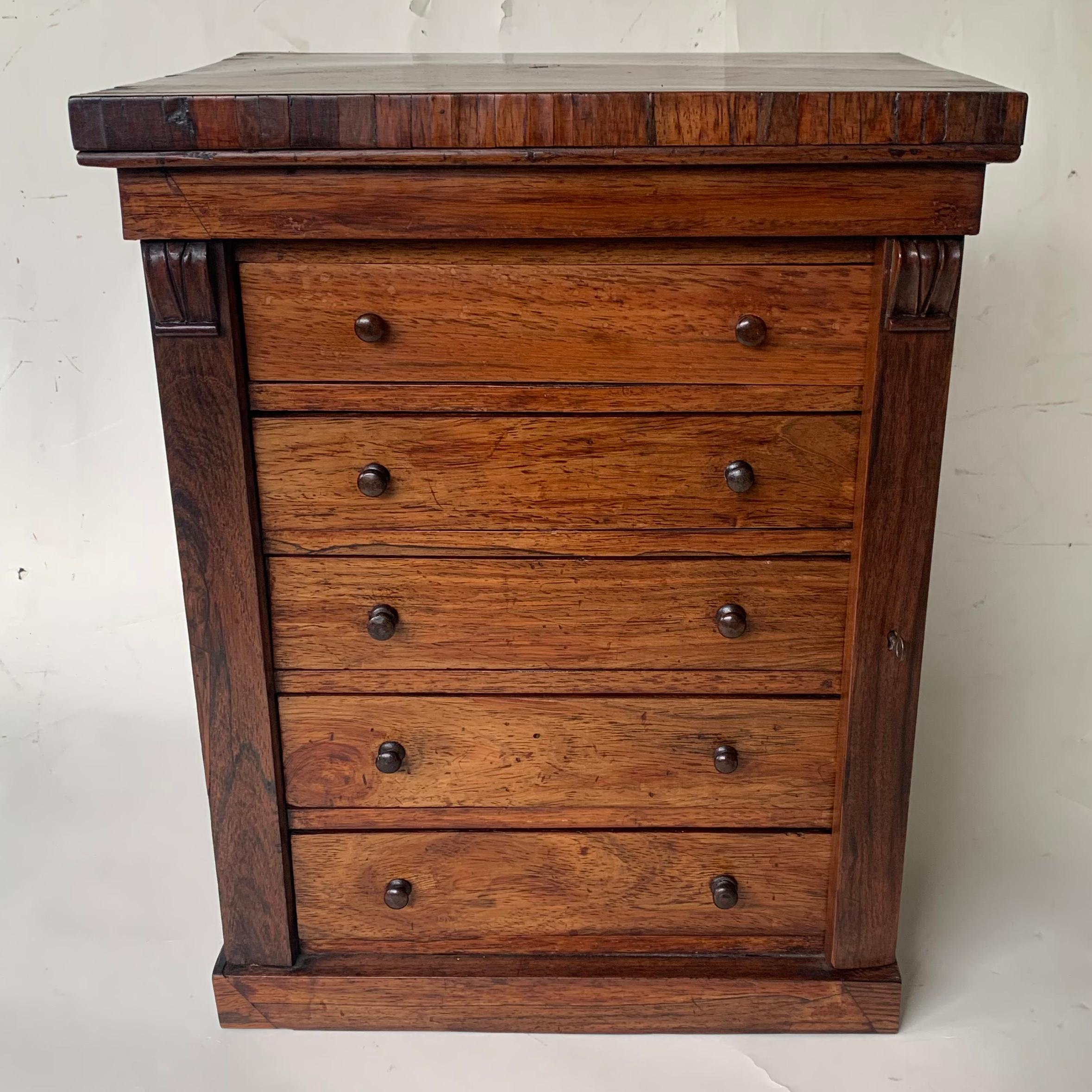 A charming early 19th century rosewood five drawer miniature Wellington chest with a stepped rectangular top above five graduated drawers which are all locked by the hinged side pilaster on the right, and standing on a plain plinth base.